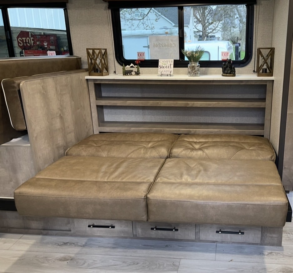 Cozy RV rental interior featuring a tan convertible sofa bed, storage shelves, and decorative touches, perfect for a comfortable journey.. Keystone RV Springdale Classic 2025