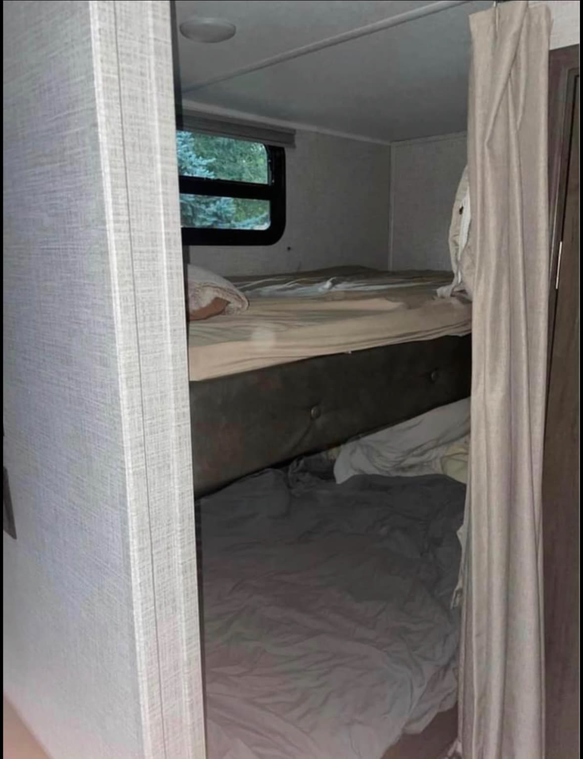 Inside an RV rental: cozy bunk beds with window views of trees and a privacy curtain. Perfect for travel accommodations.. East to West Della Terra 2021