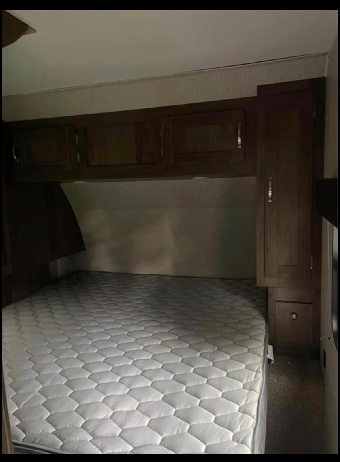 Cozy RV rental bedroom features a comfortable quilted mattress, overhead storage cabinets, and a bedside wardrobe.. East to West Della Terra 2021