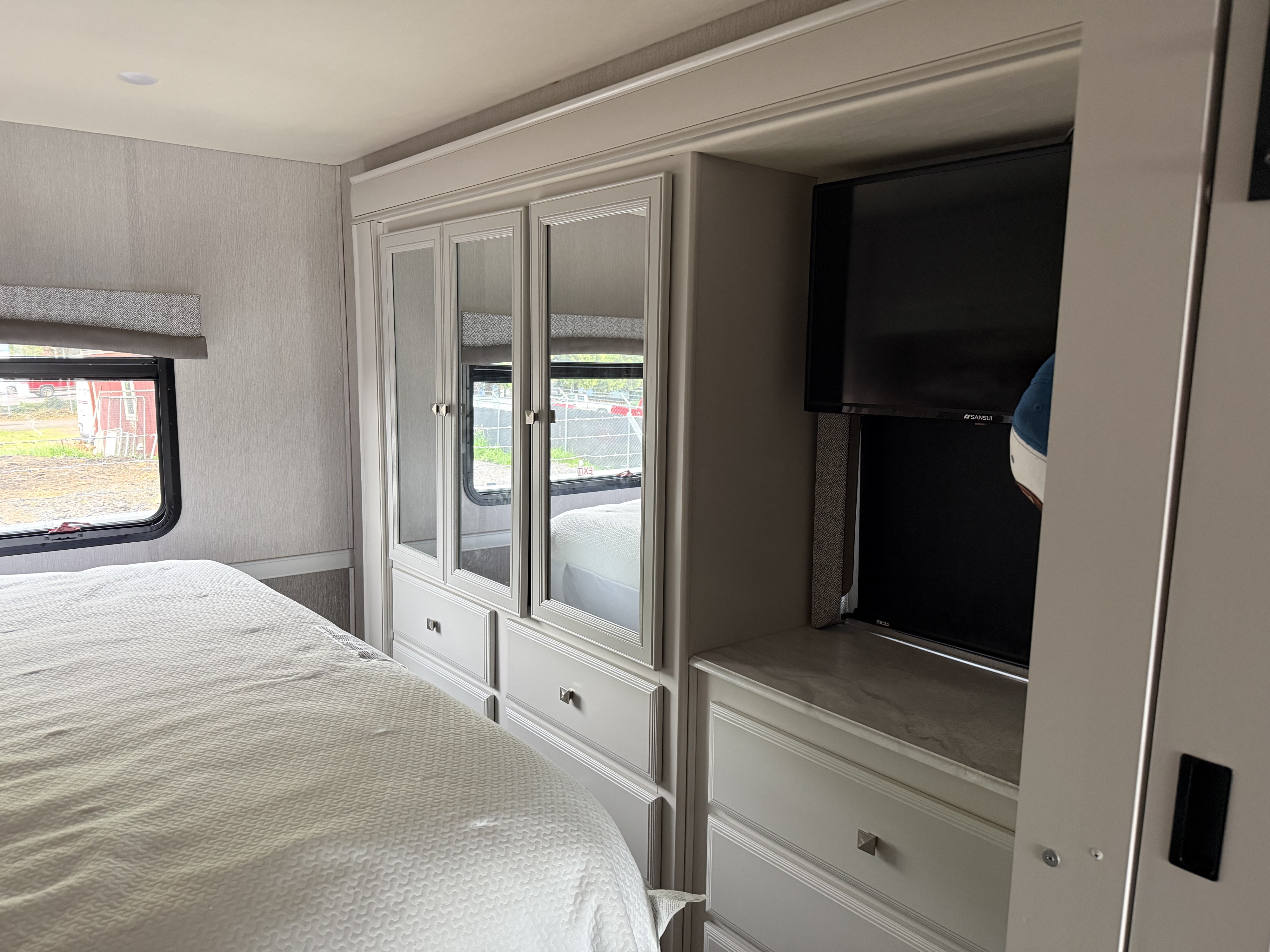 Modern RV rental bedroom featuring a TV, mirrored wardrobe, ample storage, and a cozy bed by a window.. Fleetwood Flair 2021