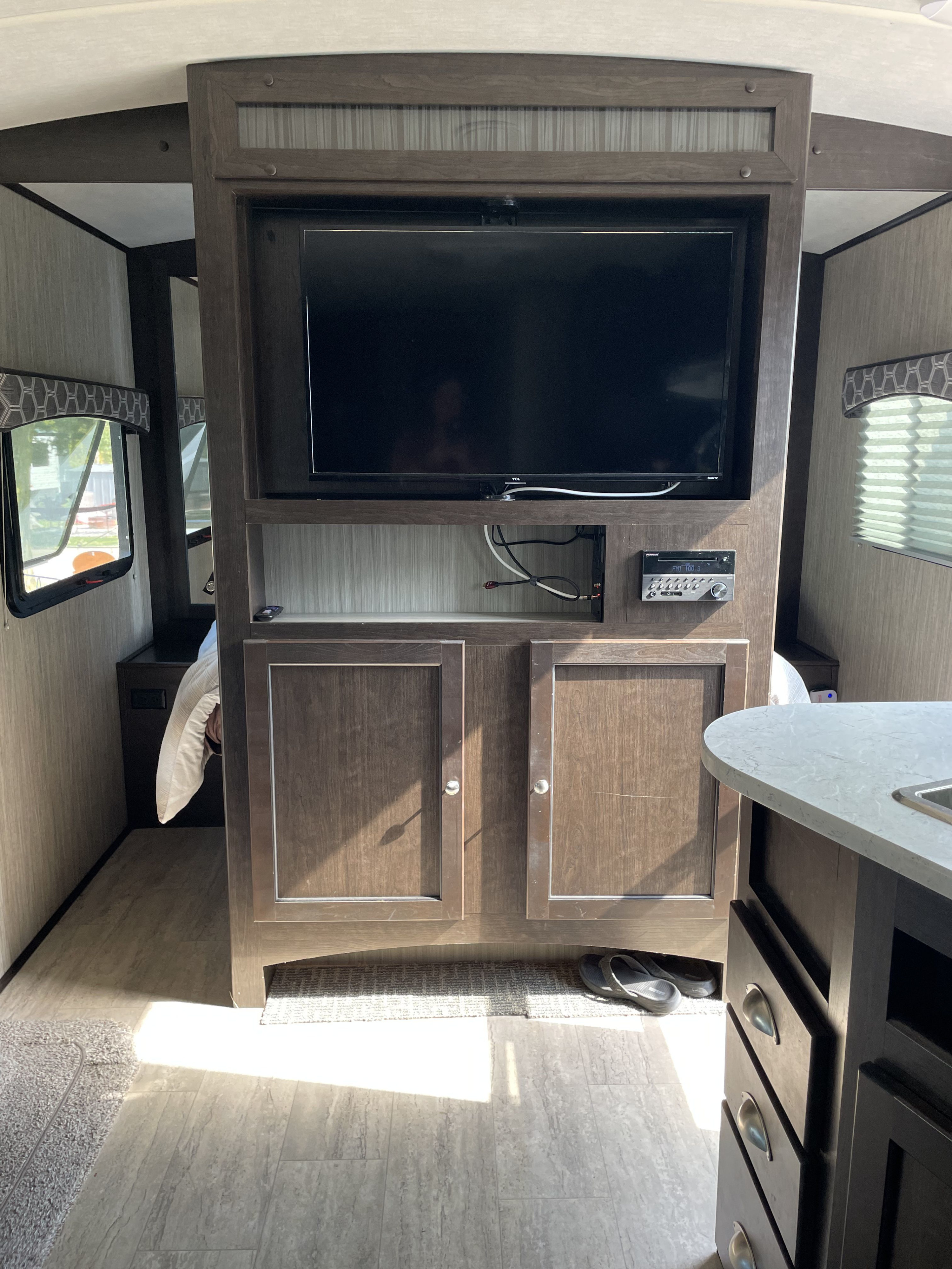 Bright RV rental interior showing a central TV console, cozy bed nook, and partial kitchen counter with modern finishes.. Cruiser RV Shadow Cruiser 2020