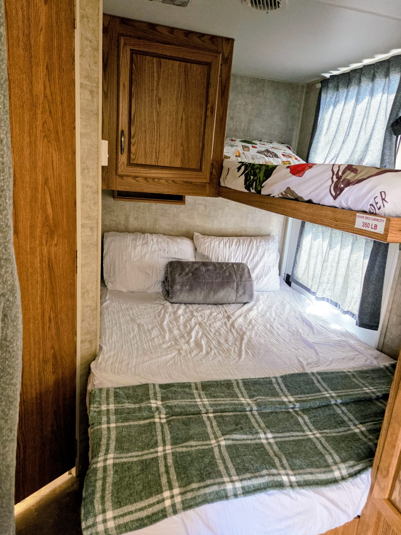 Cozy RV rental sleeping area showing bunk beds above a main bed, with wooden cabinets and window curtains for privacy.. Prowler Prowler Fifth Wheel 2006