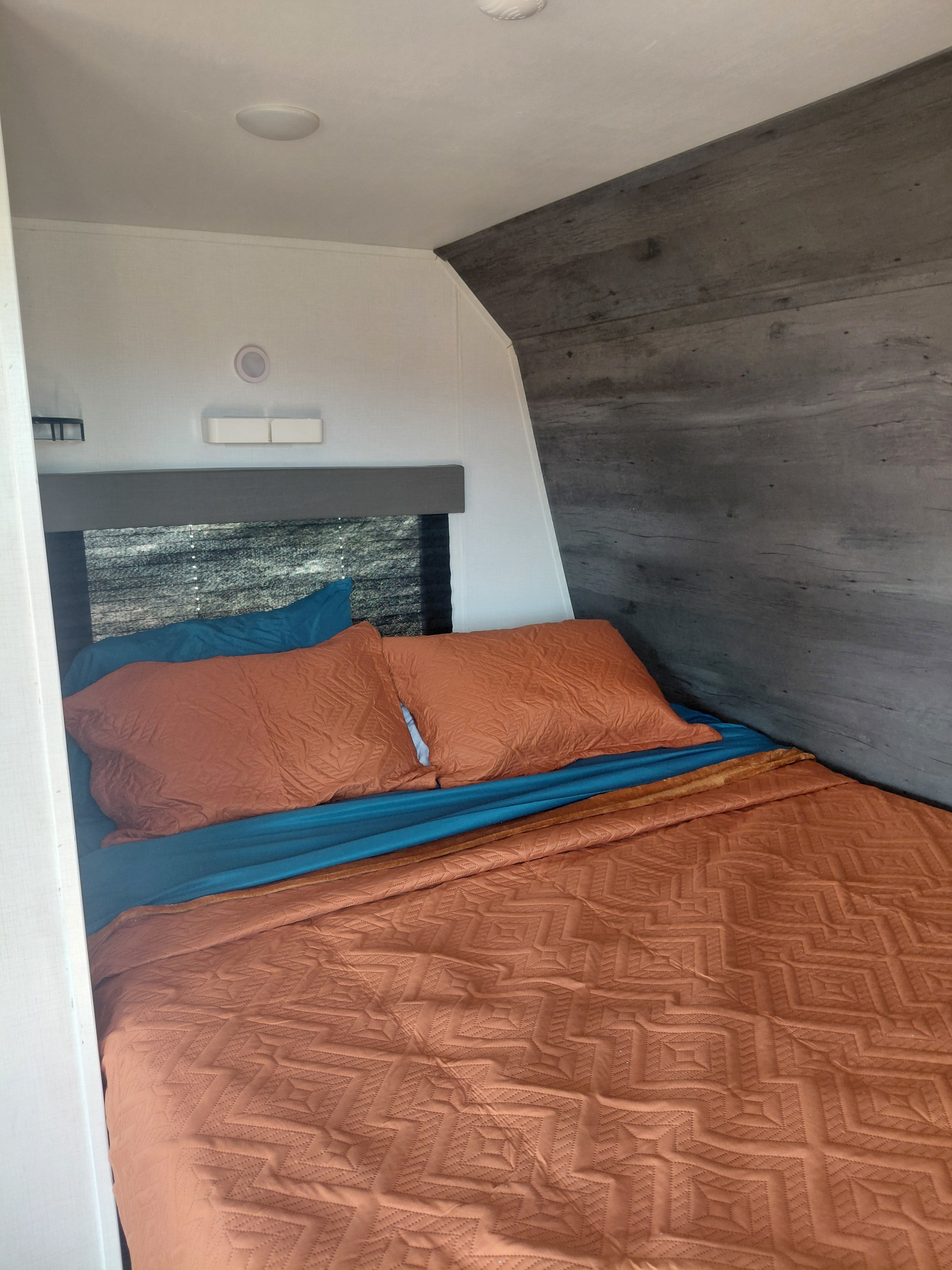 Cozy RV rental bedroom with orange quilted bedding, blue sheets, and modern decor, perfect for travel accommodations.. Keystone RV Hideout 2022