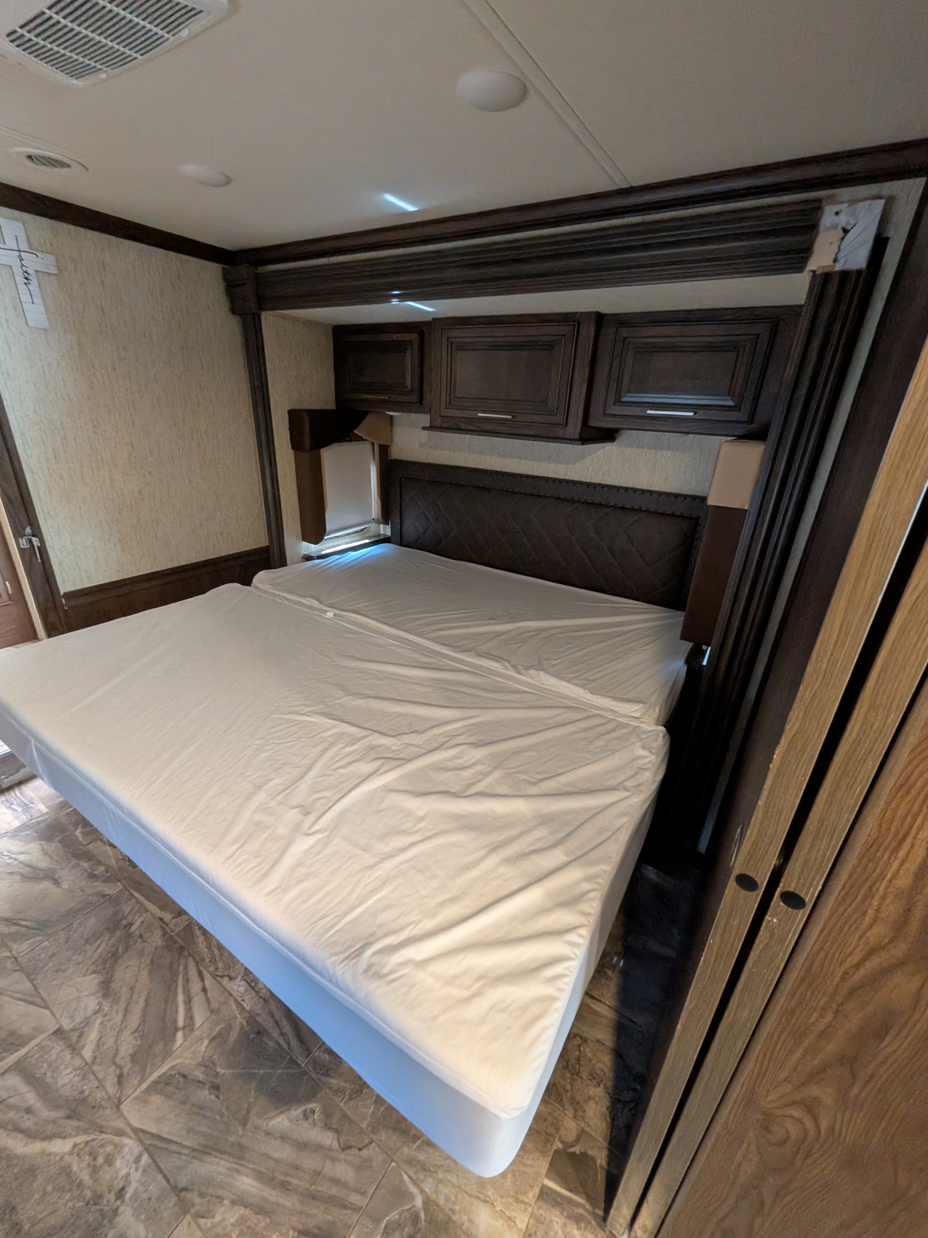 Spacious RV rental bedroom with a split bed, dark wood overhead cabinets, and an upholstered headboard on a patterned floor.. Forest River Coachmen Sportscoach SRS 2020