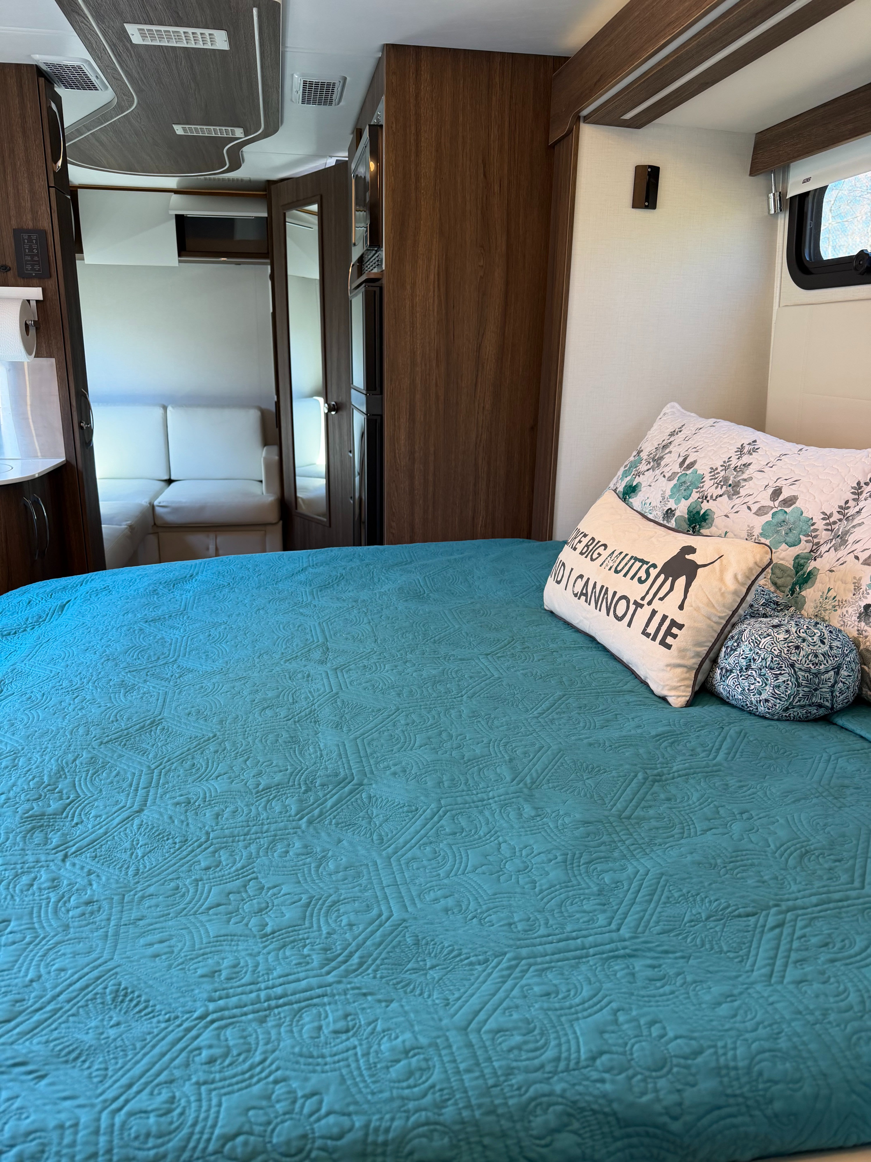 Comfortable rv rental interior: bedroom with teal quilt, fun dog pillow, and compact living area beyond.. Leisure Travel Vans Unity 2023