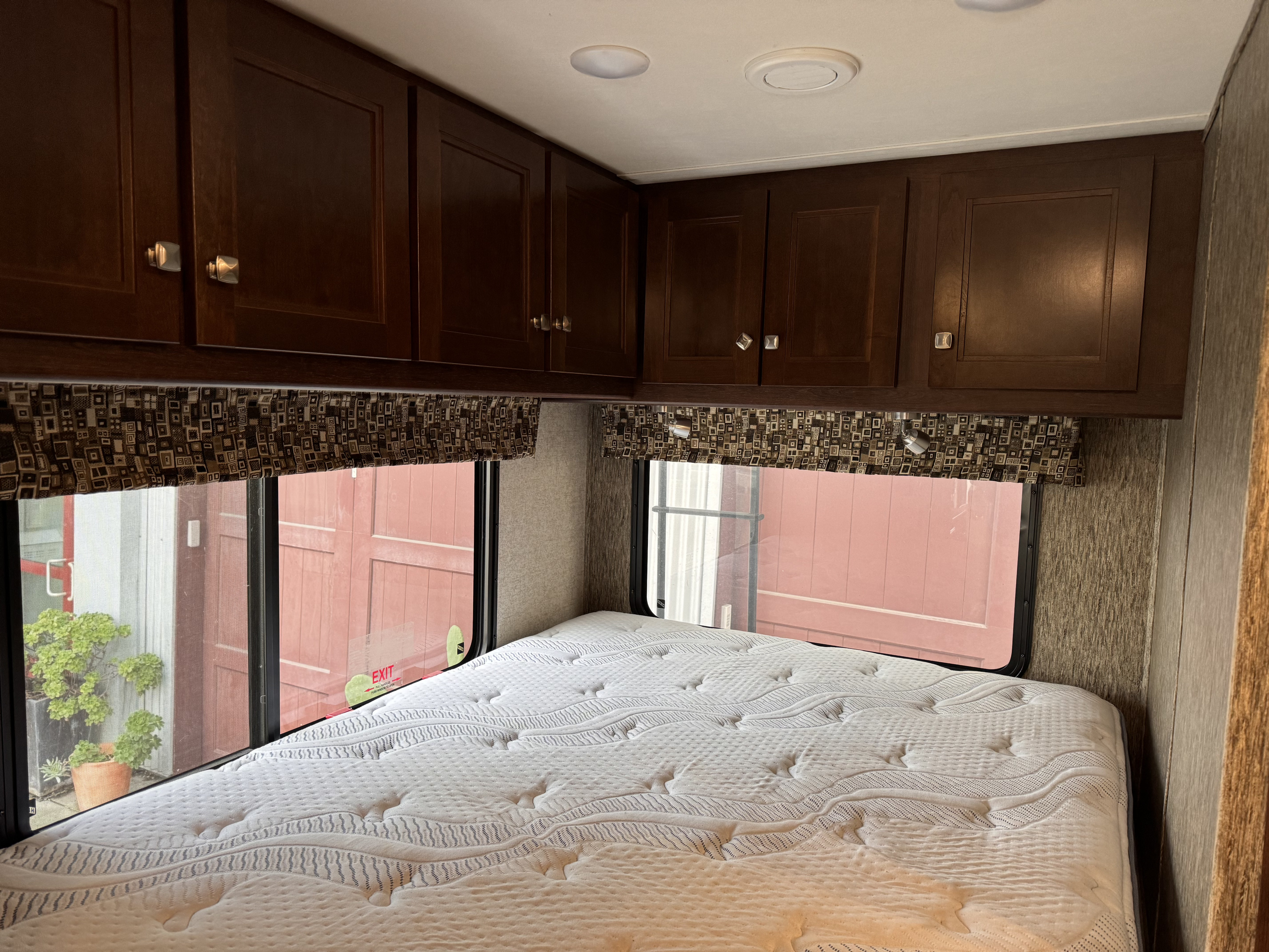 Enjoy a comfortable sleep in this RV rental bedroom with a plush mattress, dark wood cabinets, and large windows.. Forest River Sunseeker MBS 2017