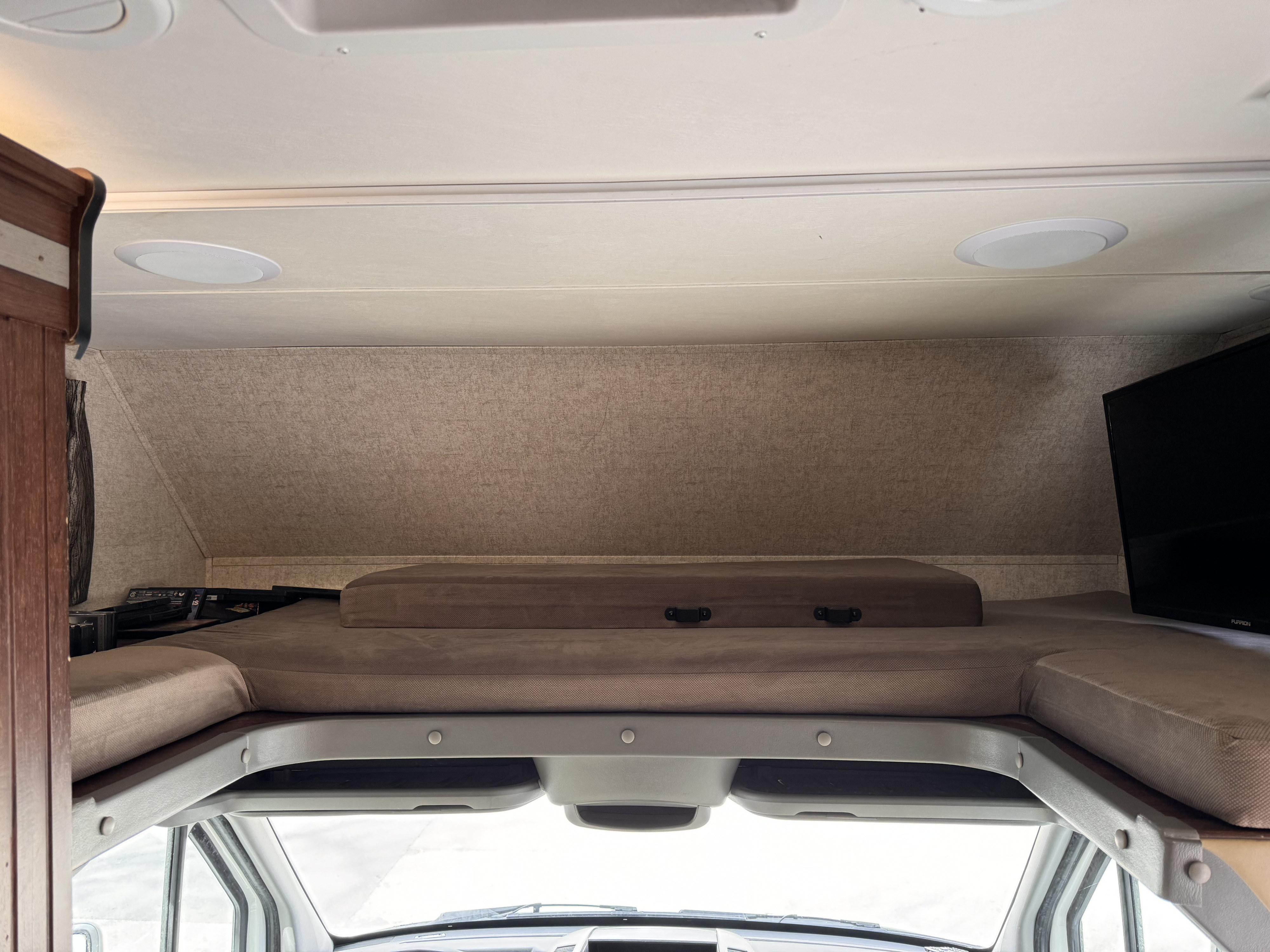 RV rental's cab-over bunk bed with mattresses, built-in speakers, and TV, offering cozy extra sleeping space.. Forest River Sunseeker MBS 2017