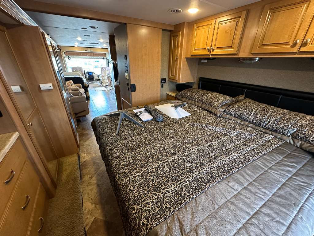 Experience comfort in this cozy RV rental bedroom featuring patterned bedding, wood cabinets, and a clear view to the living space.. Thor Miramar 2016