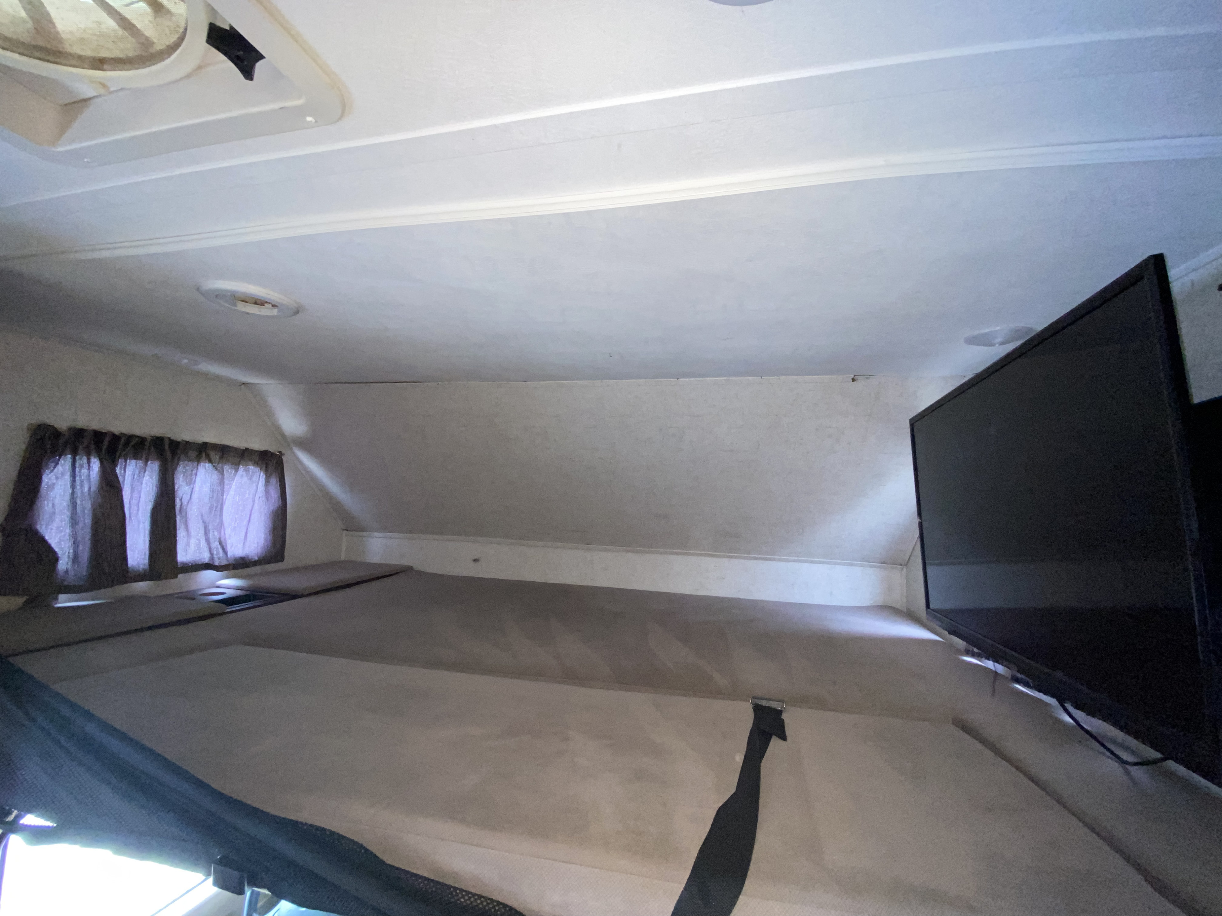 Cozy RV rental sleeping bunk featuring a comfortable bed, TV, and window with curtains, creating a restful travel space.. Forest River Sunseeker 2017