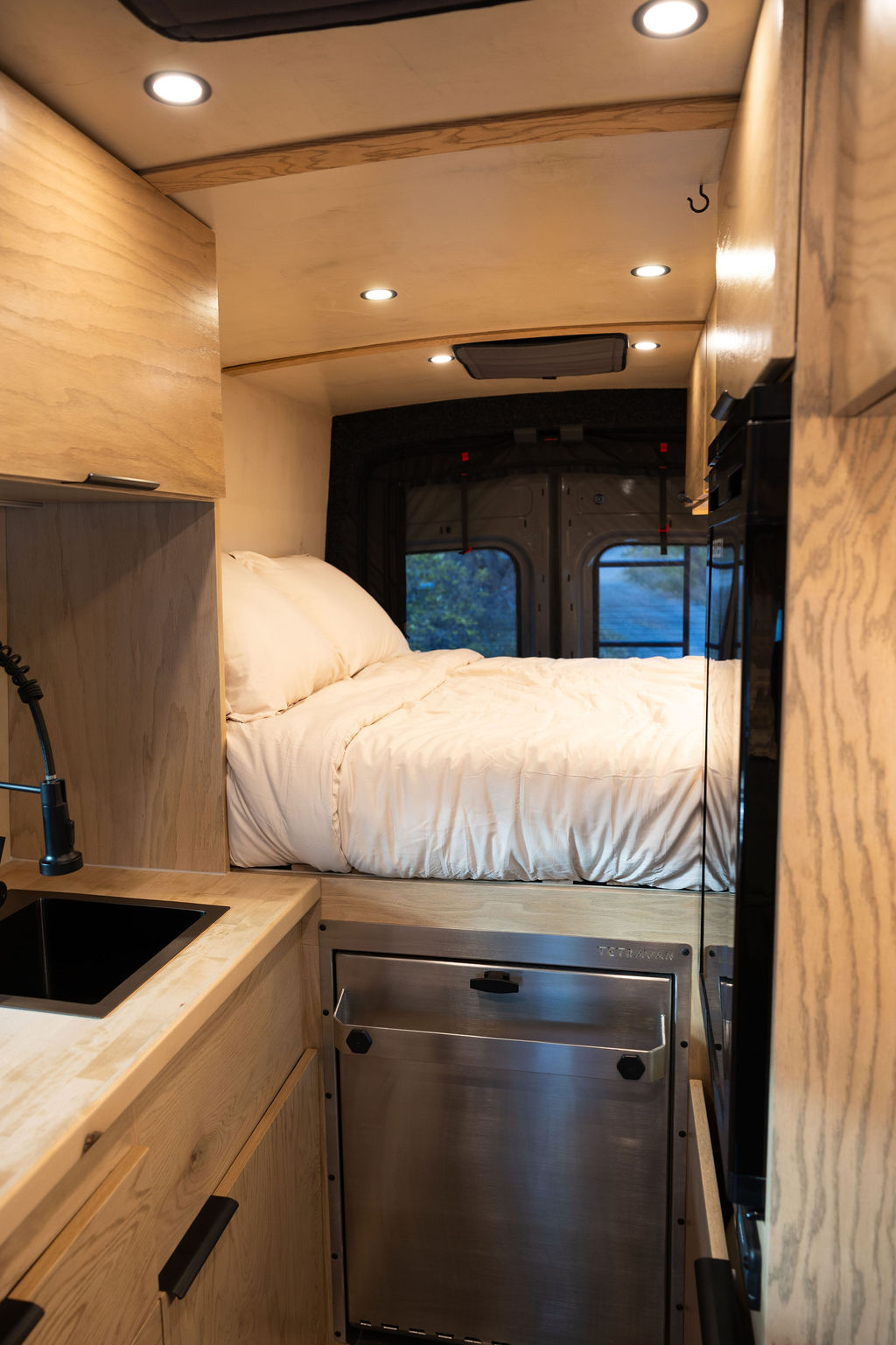 Modern RV rental camper van interior featuring a sleek kitchen, cozy bed, and custom wooden cabinetry. Perfect for vanlife adventures.. Ford Transit 2022