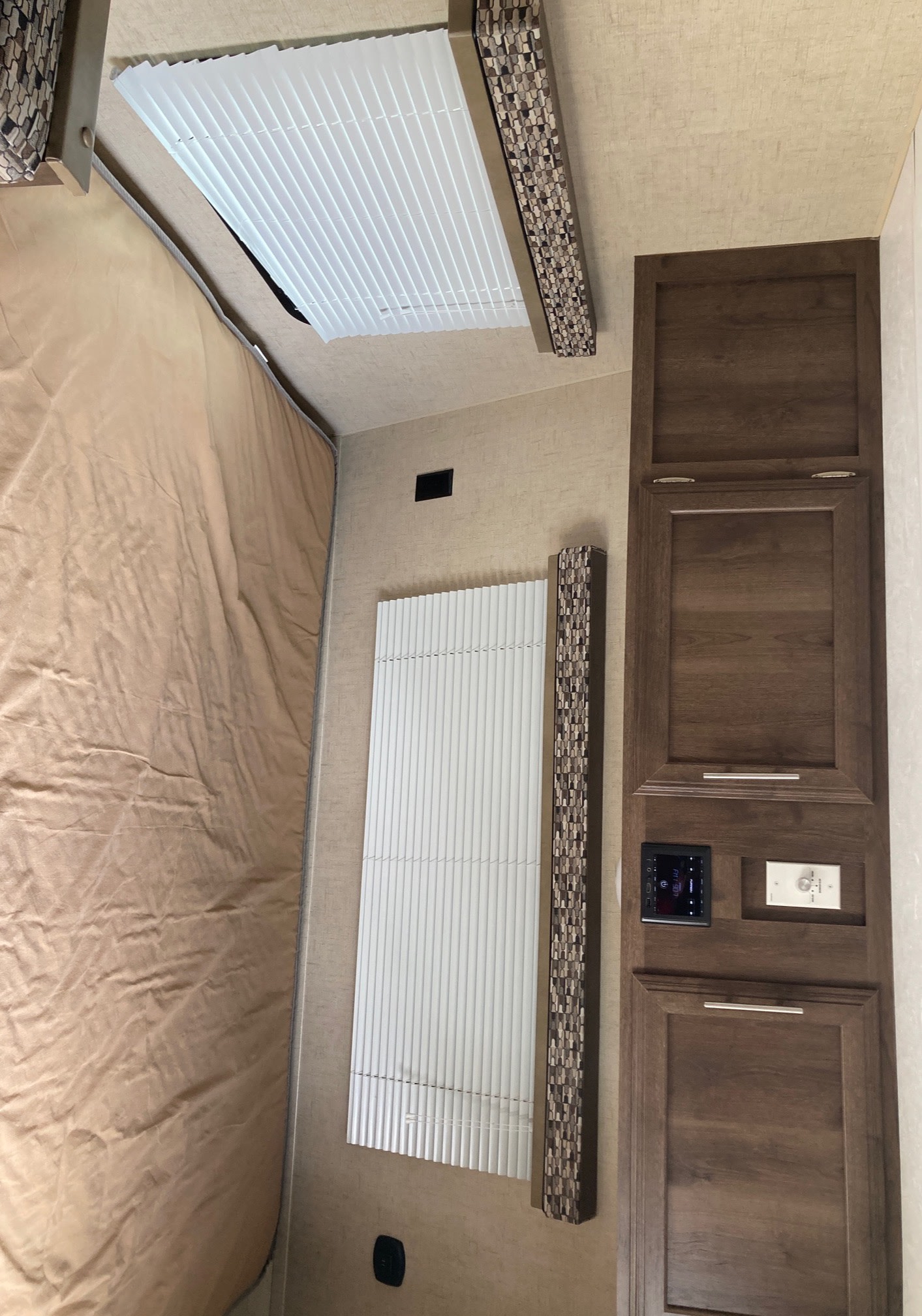 Inside an RV rental, a cozy bedroom with a tan bed, wood overhead cabinets, and windows with white blinds.. KZ Escape 2017
