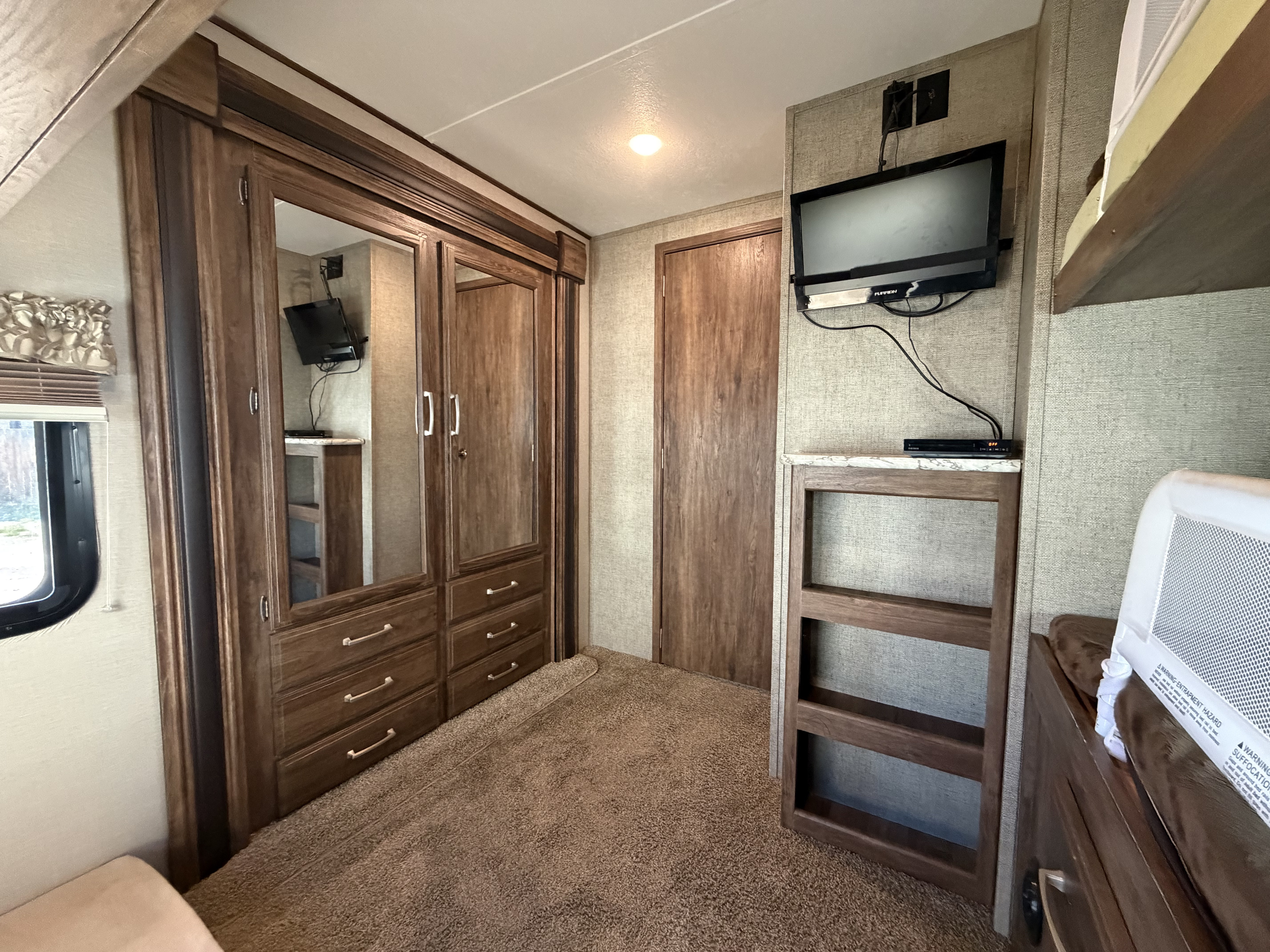 RV rental interior: A practical bedroom setup featuring a wardrobe, TV, bunk bed, and plush carpeting.. Keystone RV Cougar 2017