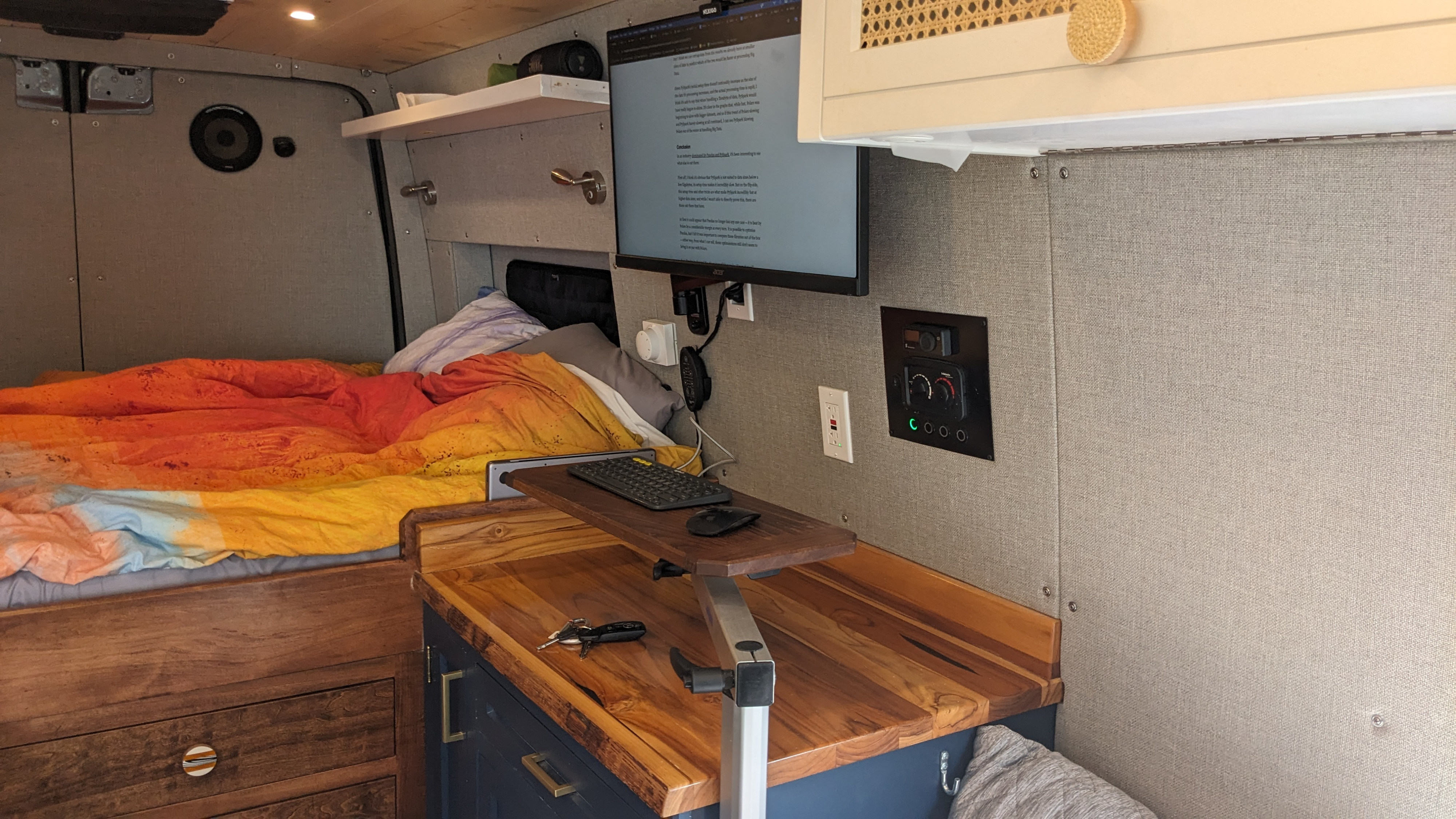 Well-equipped RV rental van interior: bed, monitor workspace, and climate controls for remote work and travel.. Mercedes Sprinter 2021