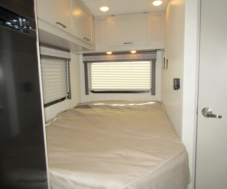 Well-lit RV rental bedroom featuring a made bed, windows with blinds, and white overhead storage cabinets.. Thor Chateau 2025