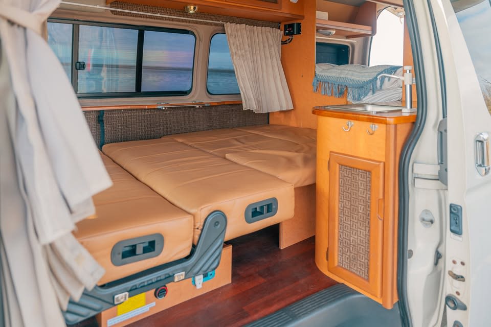 This RV rental interior features a convertible bed, mini kitchen with sink, and scenic window views for your road trip comfort.. Toyota Bus 4x4 Campervan conversion of Toyota Hiace 2007