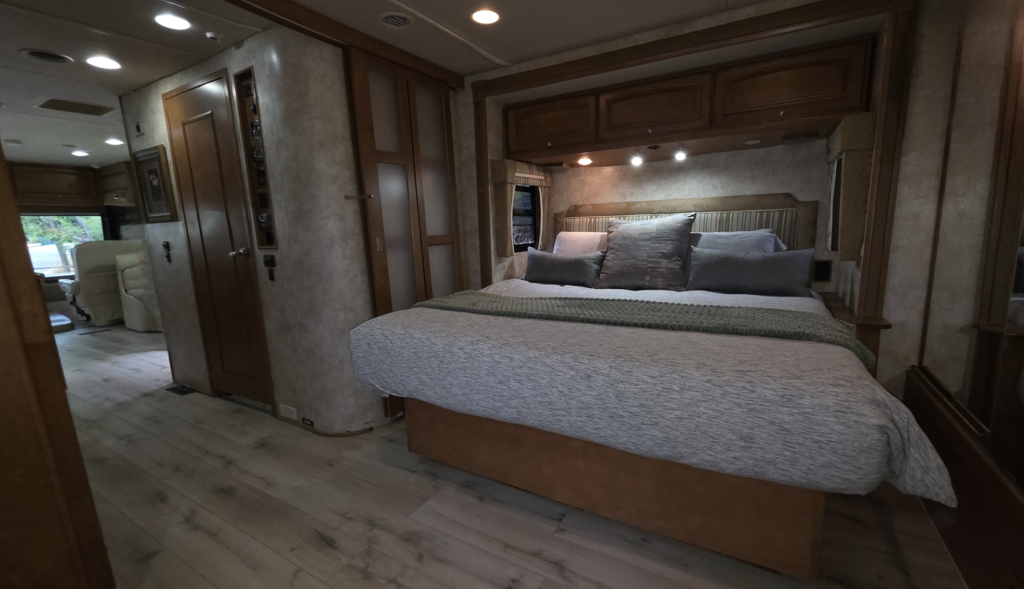 Cozy RV rental bedroom with a comfy queen bed, inviting pillows, overhead storage, and warm lighting. Ready for your journey!. Winnebago Adventurer 2012