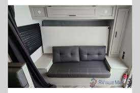 RV rental interior: A compact living area features a dark gray convertible sofa, overhead cabinets, and a window with dark blinds.. Forest River Salem FSX 2021