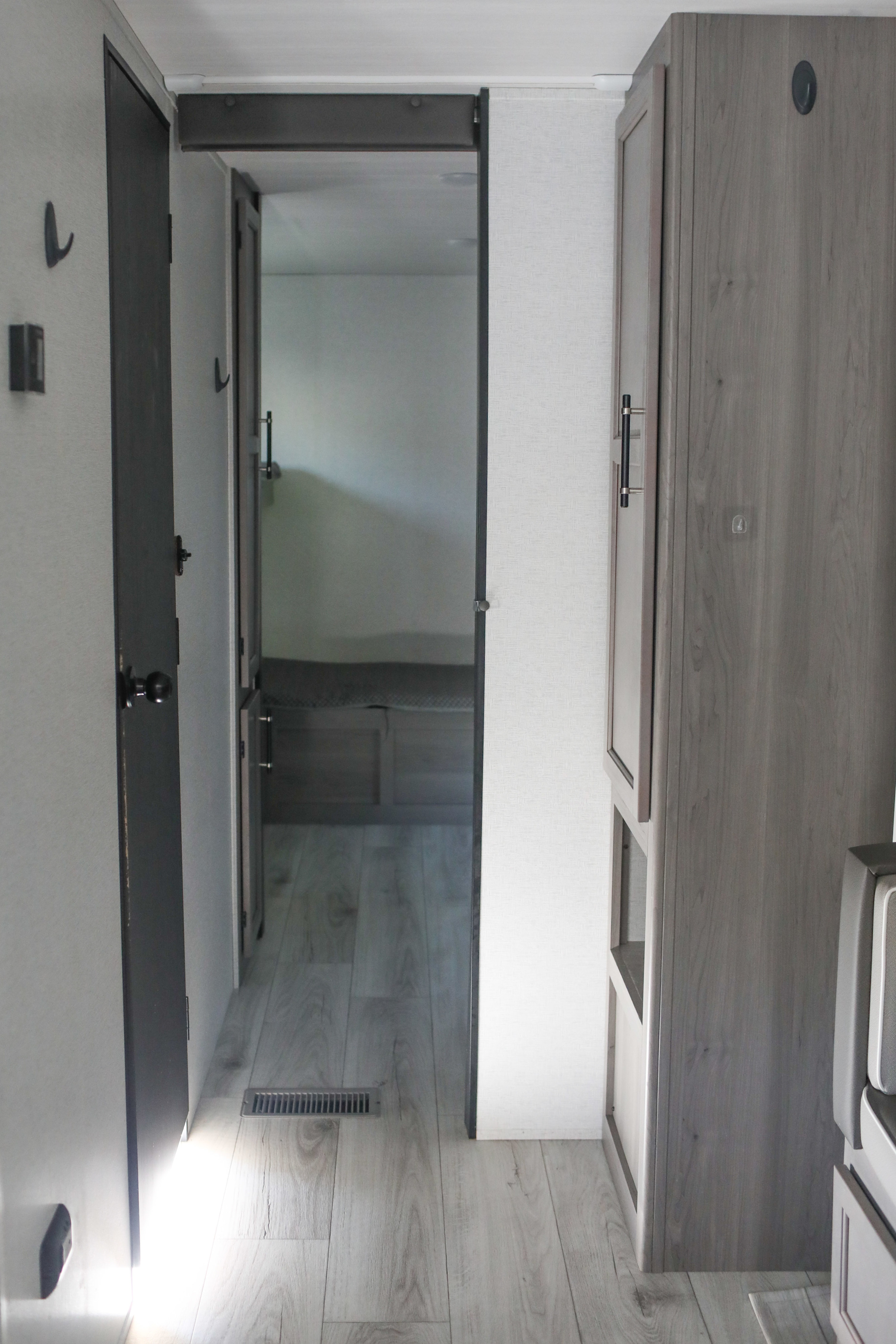 RV rental interior hallway: A modern compact space with a dark door leading to a bedroom, light wood-look flooring, and a tall storage cabinet.. Keystone RV Hideout 2025