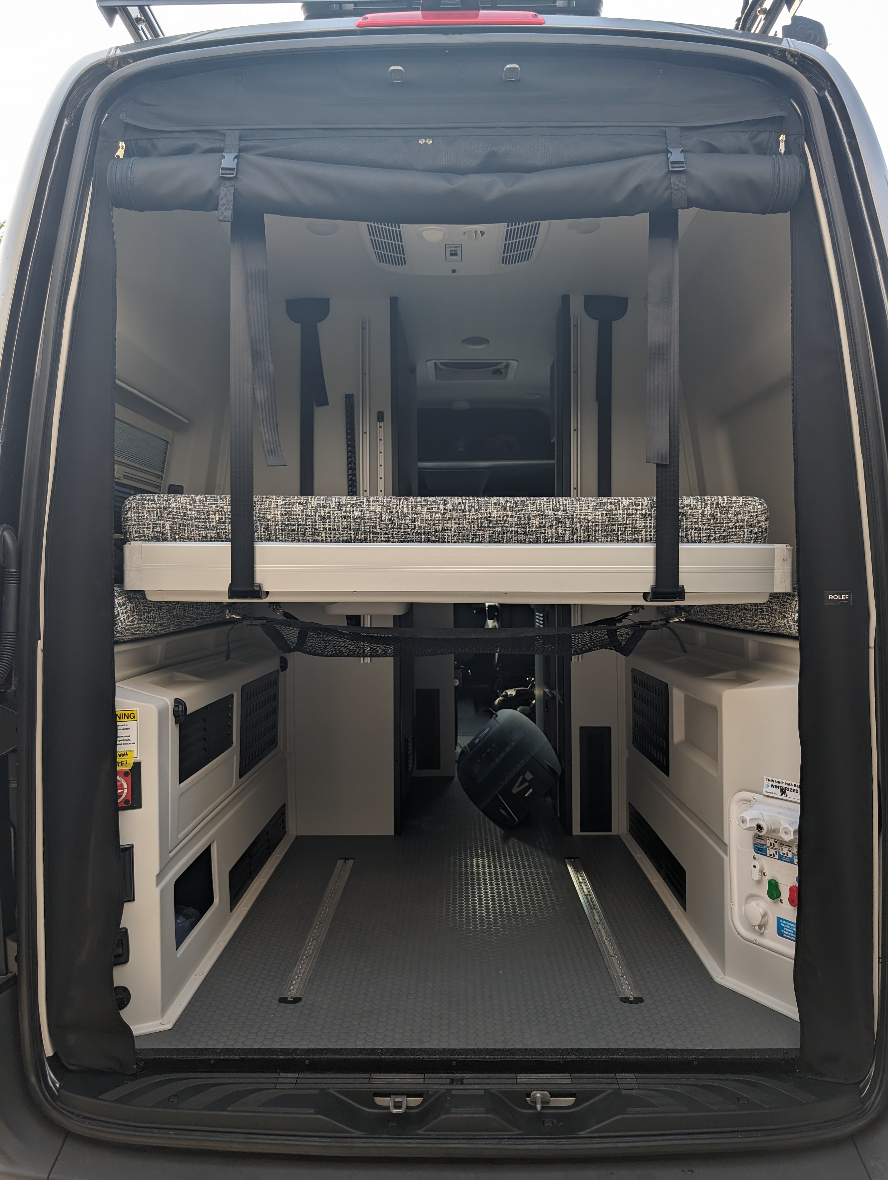 Rear view of an rv rental camper van's flexible interior, featuring a modular bed, storage, and utility connections.. Tiffin Allegro GH1 2023