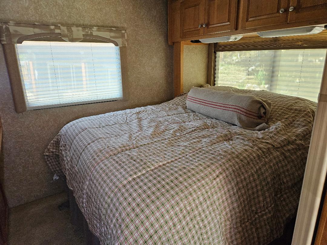 Cozy RV rental bedroom with plaid bedding, a bolster pillow, and windows with blinds, ready for a comfortable journey.. Dutchmen Dorado 2006
