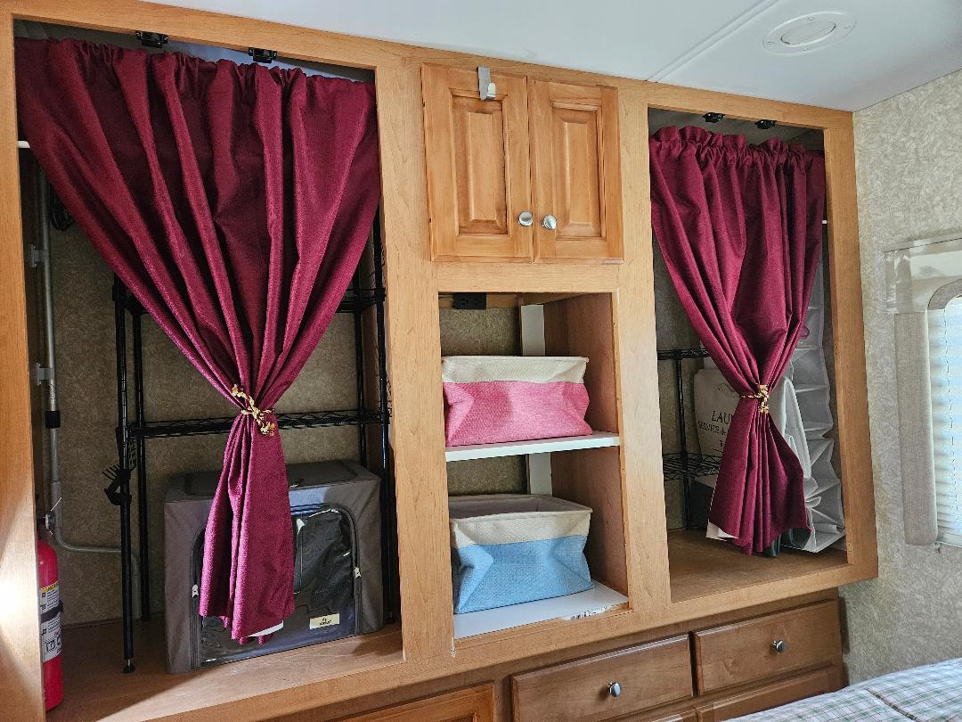 Organized RV rental storage featuring wood cabinets, shelves, colorful bins, and red tie-back curtains.. Dutchmen Dorado 2006
