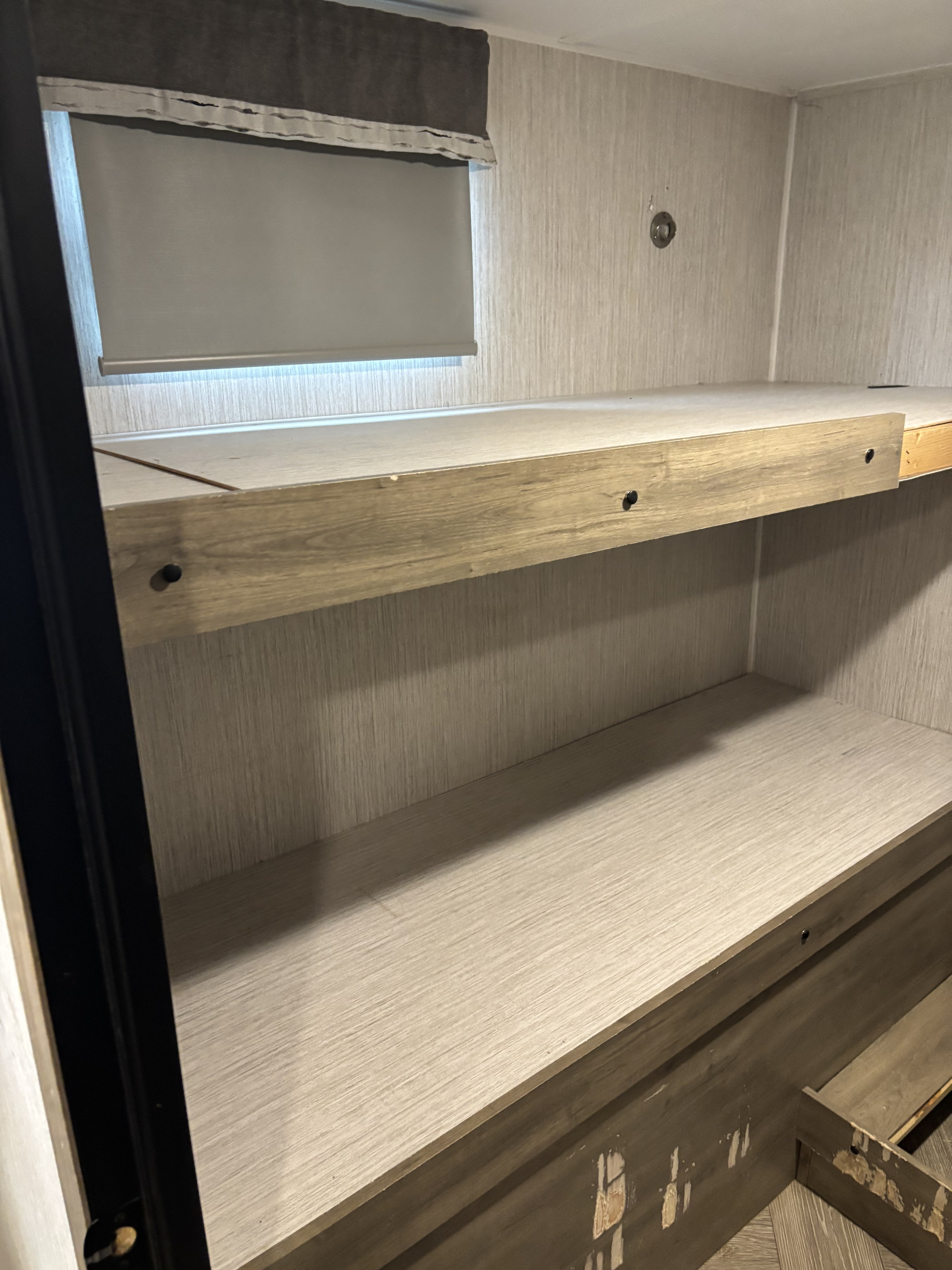 RV rental bunk area with light wood interior, window shade, and lower storage/bed frame, showing wear.. Palomino Puma 28bhss 2022