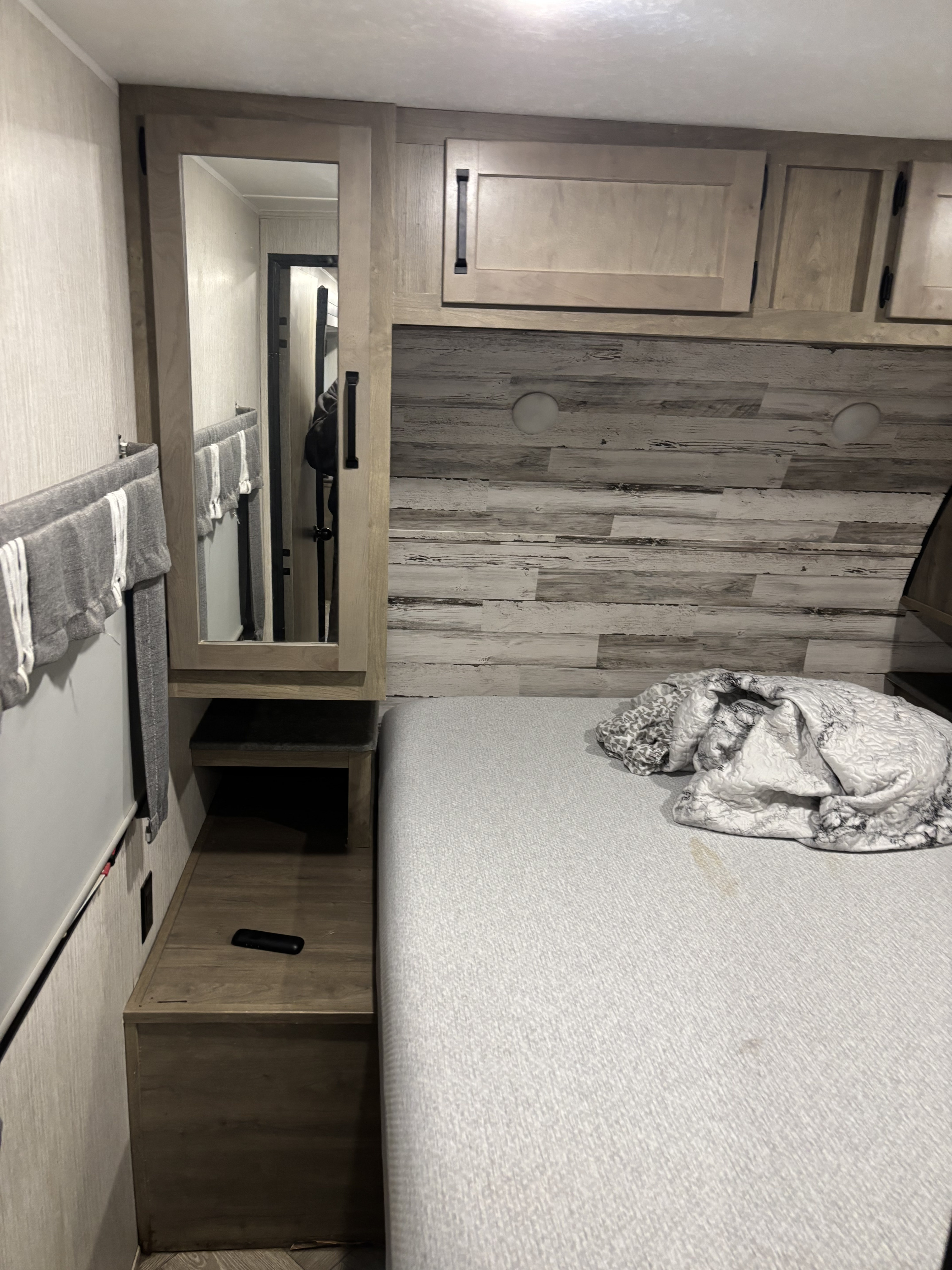 Cozy RV rental bedroom with a comfortable bed, mirrored cabinet, overhead storage, and rustic wood-paneled accent wall.. Palomino Puma 28bhss 2022