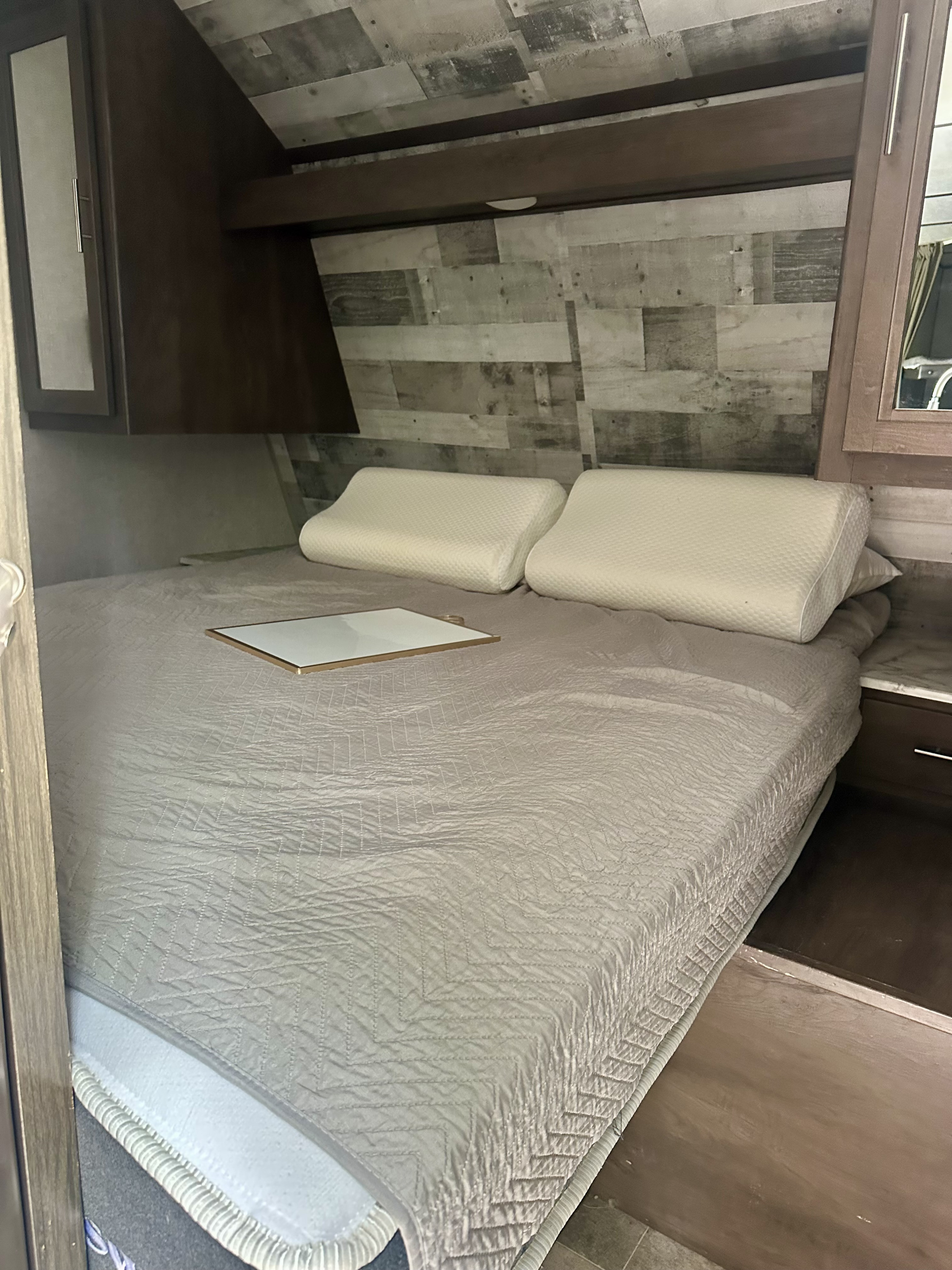 RV rental bedroom with a chevron-quilted bed, contour pillows, and rustic wood-paneled walls.. Dutchmen Coleman Lantern 2020