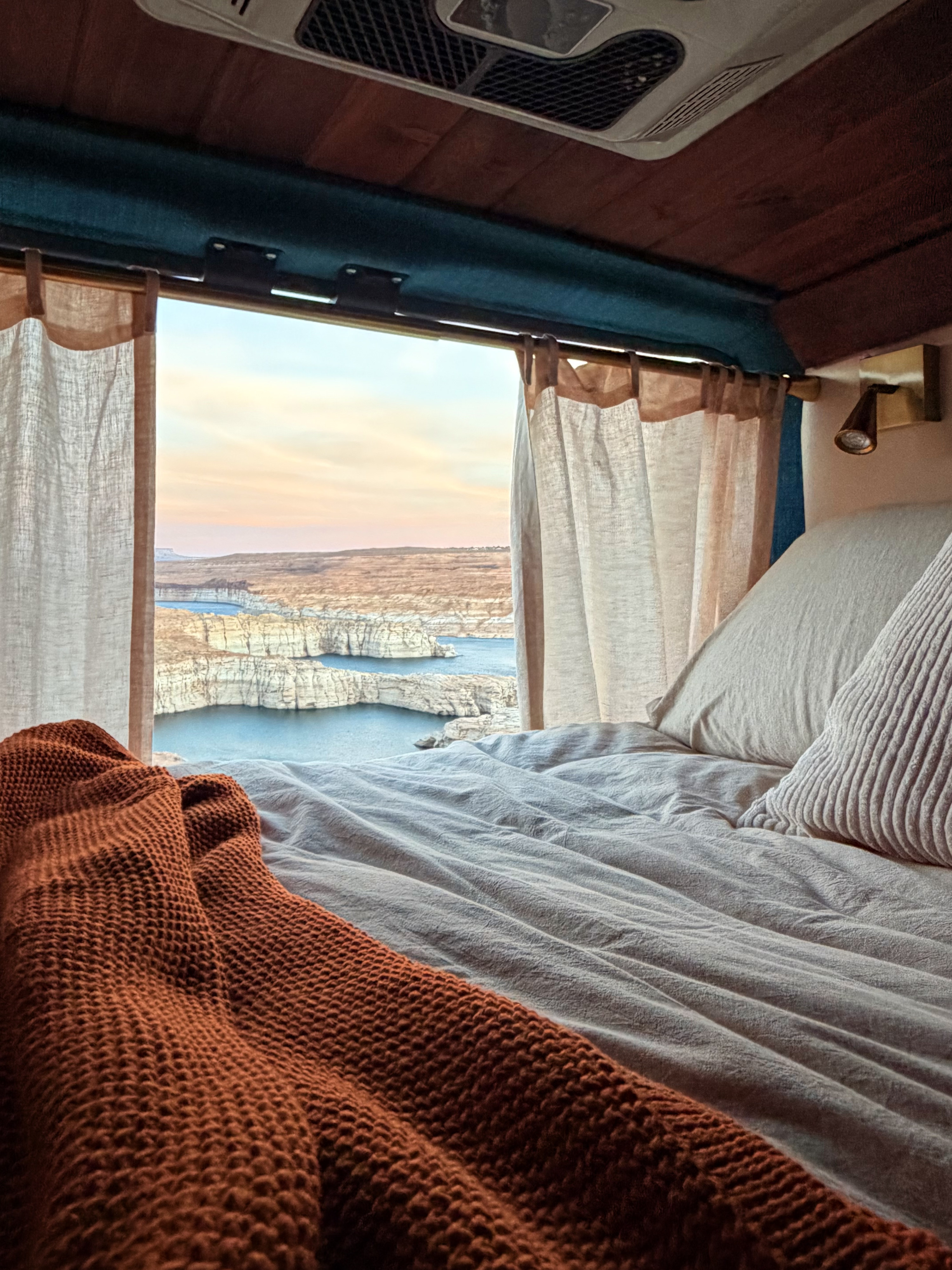 Relax in this cozy RV rental bed, offering expansive views of a lake nestled within rocky canyons at sunrise/sunset.. Dodge Promaster 2500 2021