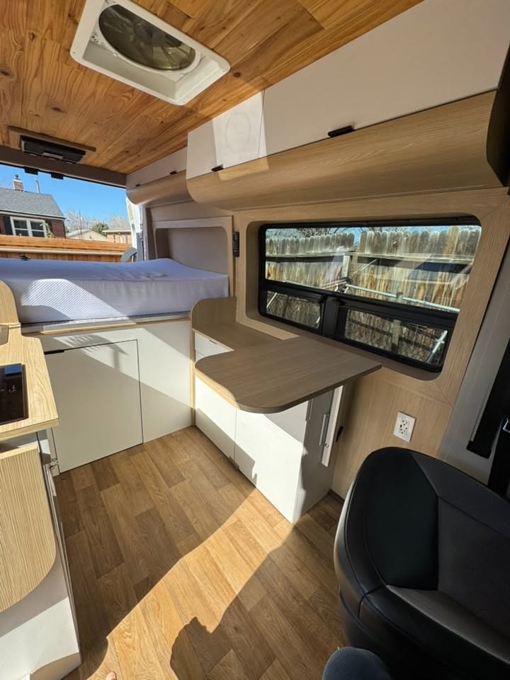 Modern RV rental interior: wood-paneled ceiling, comfy bed, sleek cabinetry, and a functional table workspace.. Dodge 1500 2019