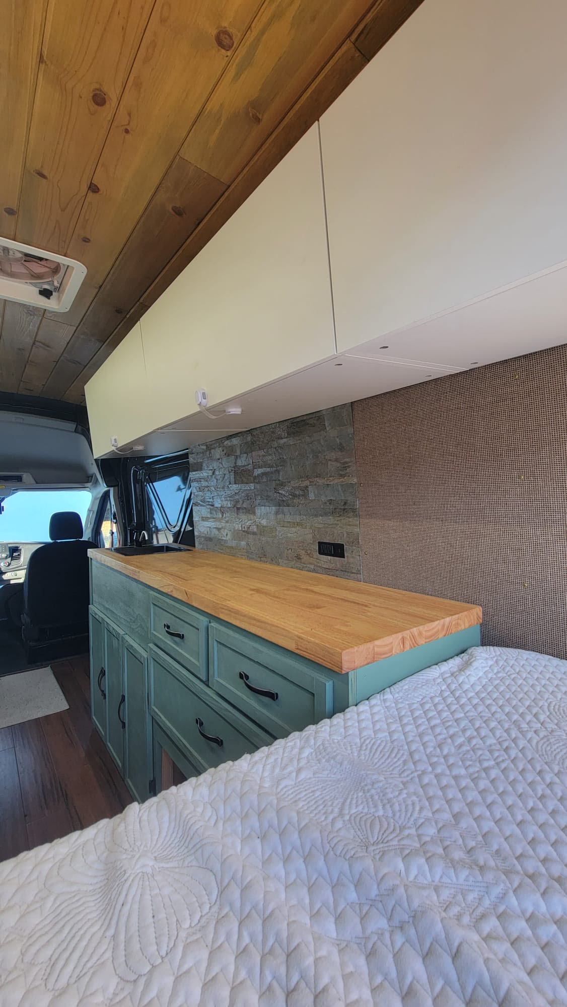 Cozy RV rental interior featuring a teal kitchenette, wooden countertop, stone backsplash, and white quilted bed.. Ford Custom Transit 2020