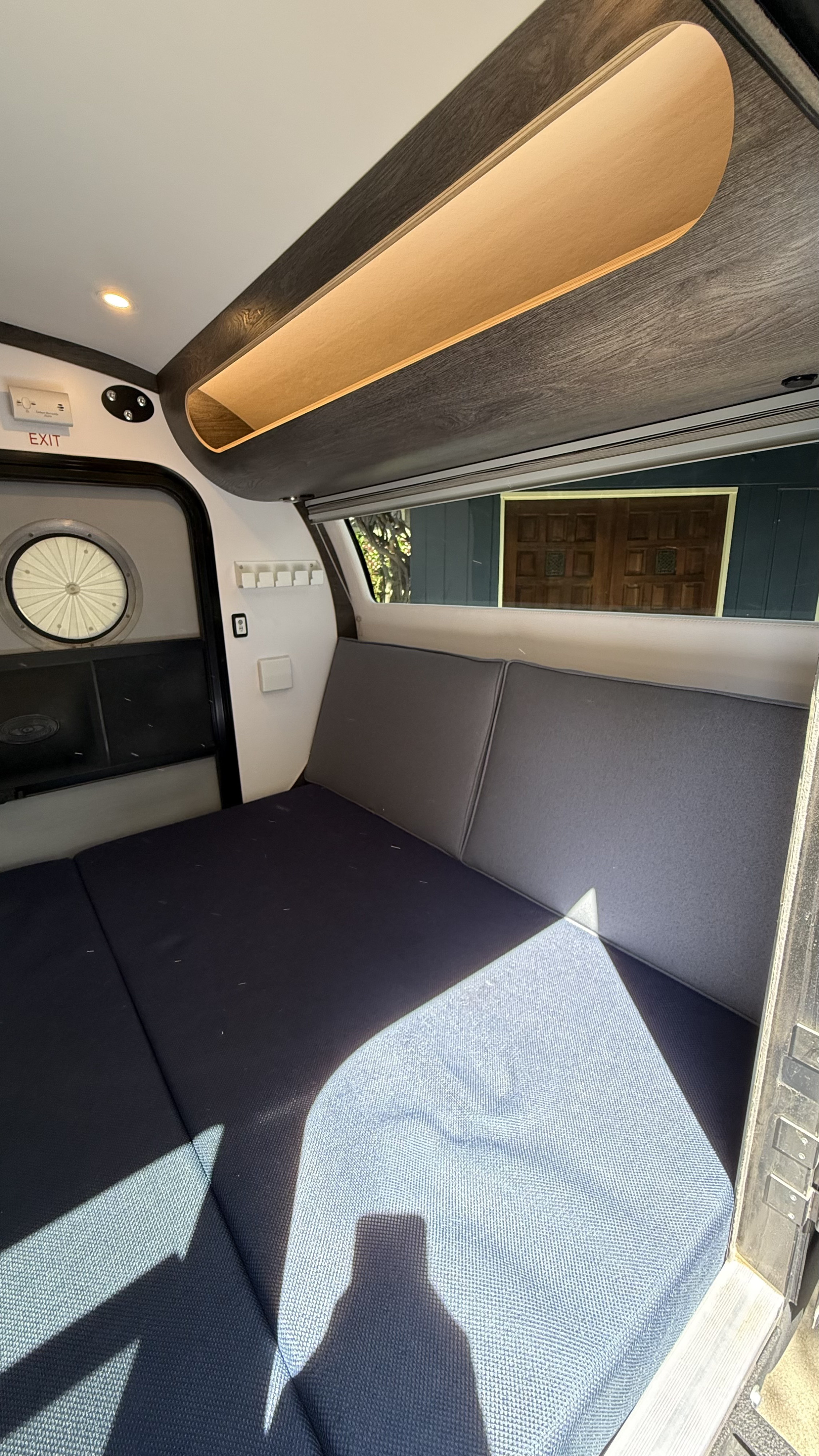 Inside an rv rental, featuring a comfortable bed with blue cushions, overhead storage, and a view outside. Ready for adventure!. Bean Trailer Bean Trailer Trailer 2022
