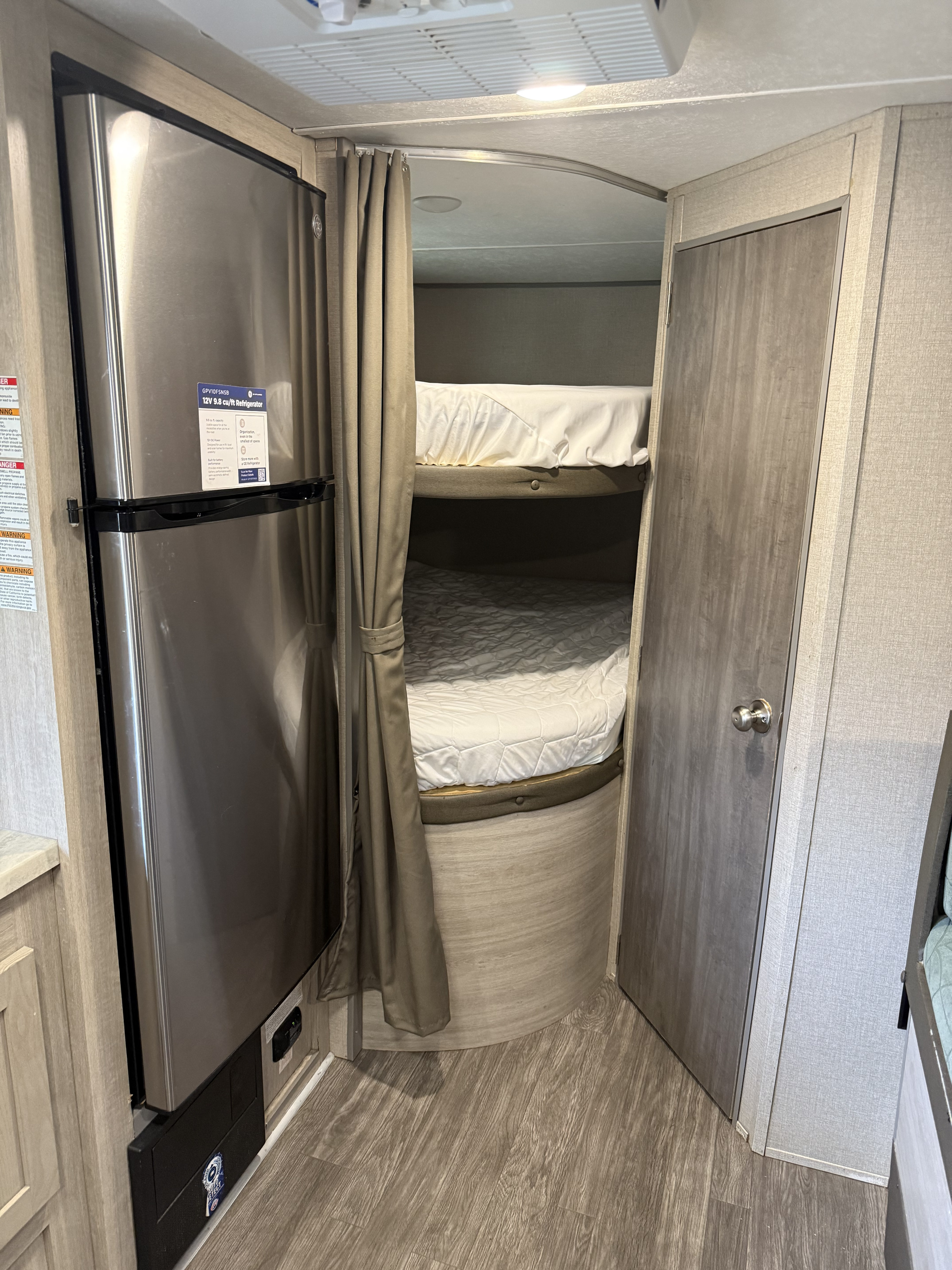 RV rental interior: stainless steel refrigerator, bunk beds with white bedding, and privacy curtain for compact sleeping.. Forest River Aurora Aurora 2022