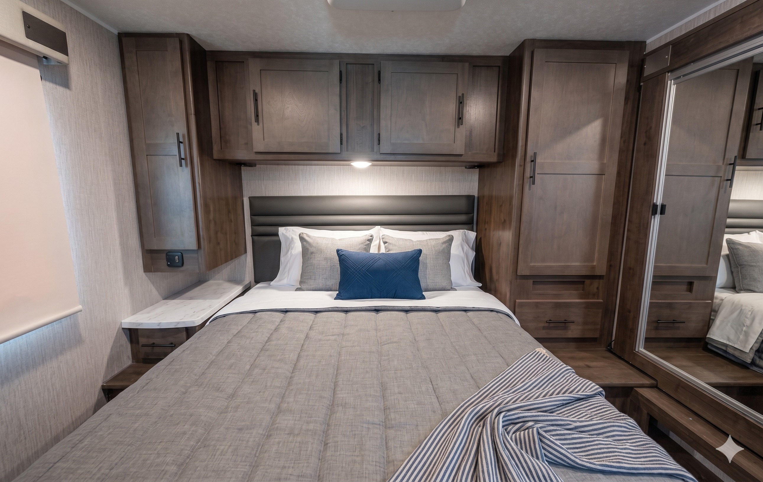 A modern, cozy RV rental bedroom featuring a comfortable bed, overhead storage, and mirrored closet doors. Perfect for travel.. Coachmen Leprechaun 2022