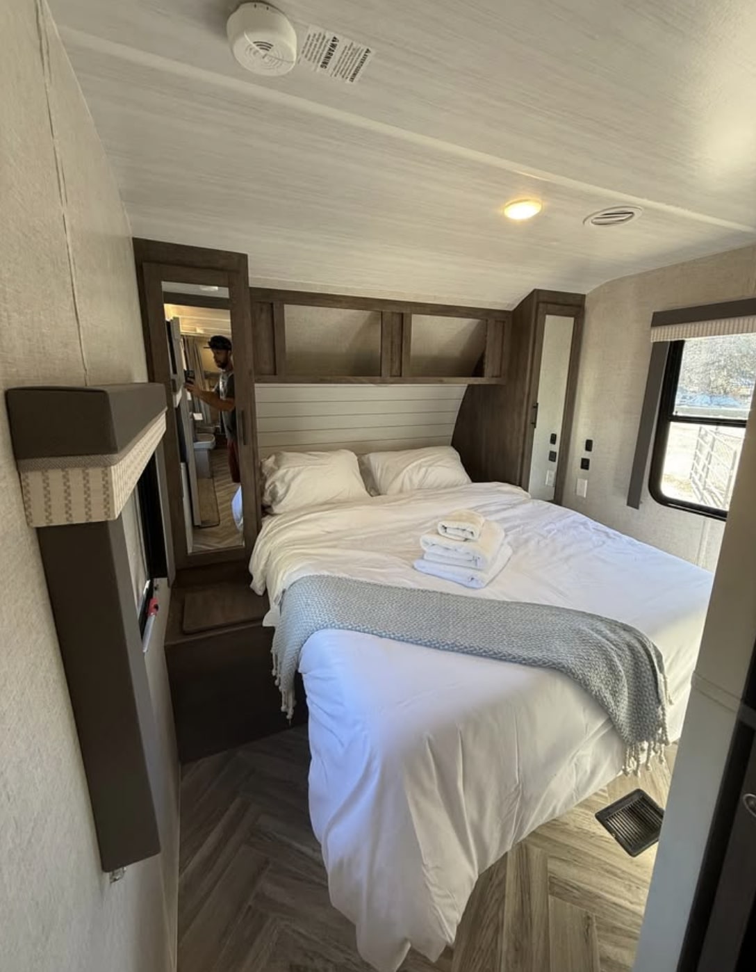 Cozy rv rental bedroom with a fresh bed, white linens, folded towels, overhead storage, and modern wood-look floor.. Forest River Salem 2022