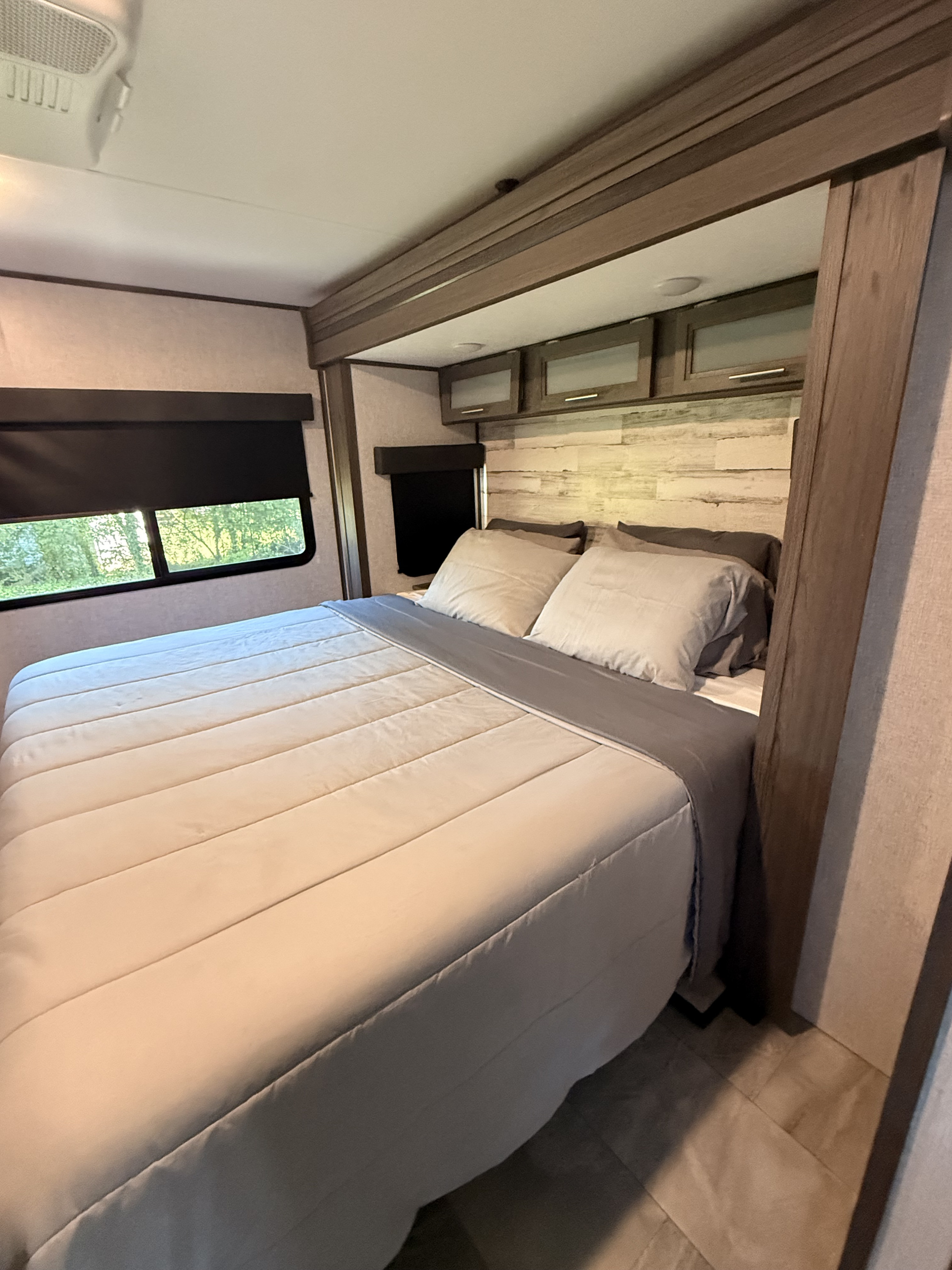 Cozy RV rental bedroom with a comfortable bed, window views, and overhead storage, ready for your next adventure.. Dutchmen Kodiak Ultimate 2021