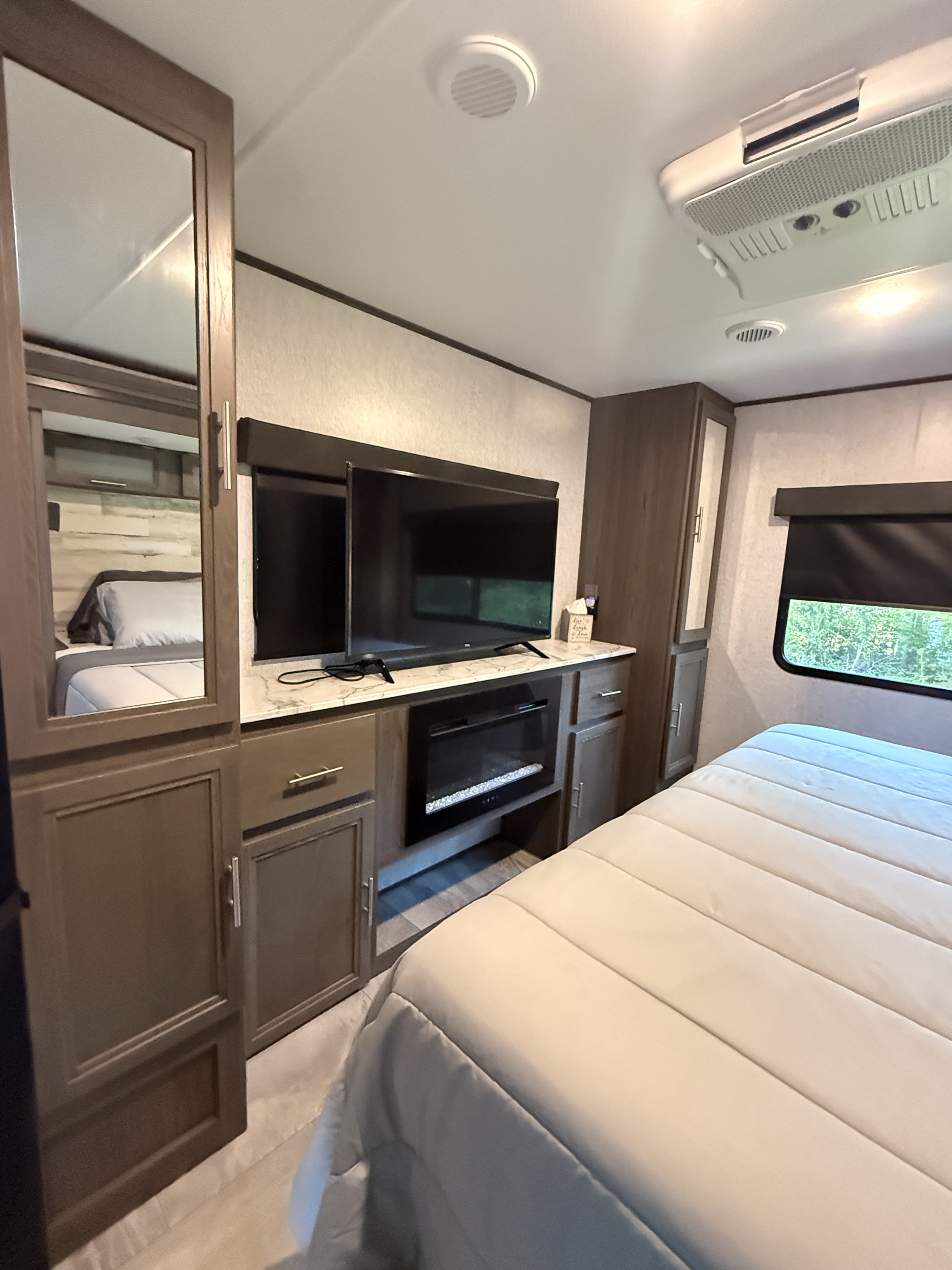 Interior of an RV rental bedroom featuring a cozy bed, entertainment unit with TV & fireplace, and storage.. Dutchmen Kodiak Ultimate 2021