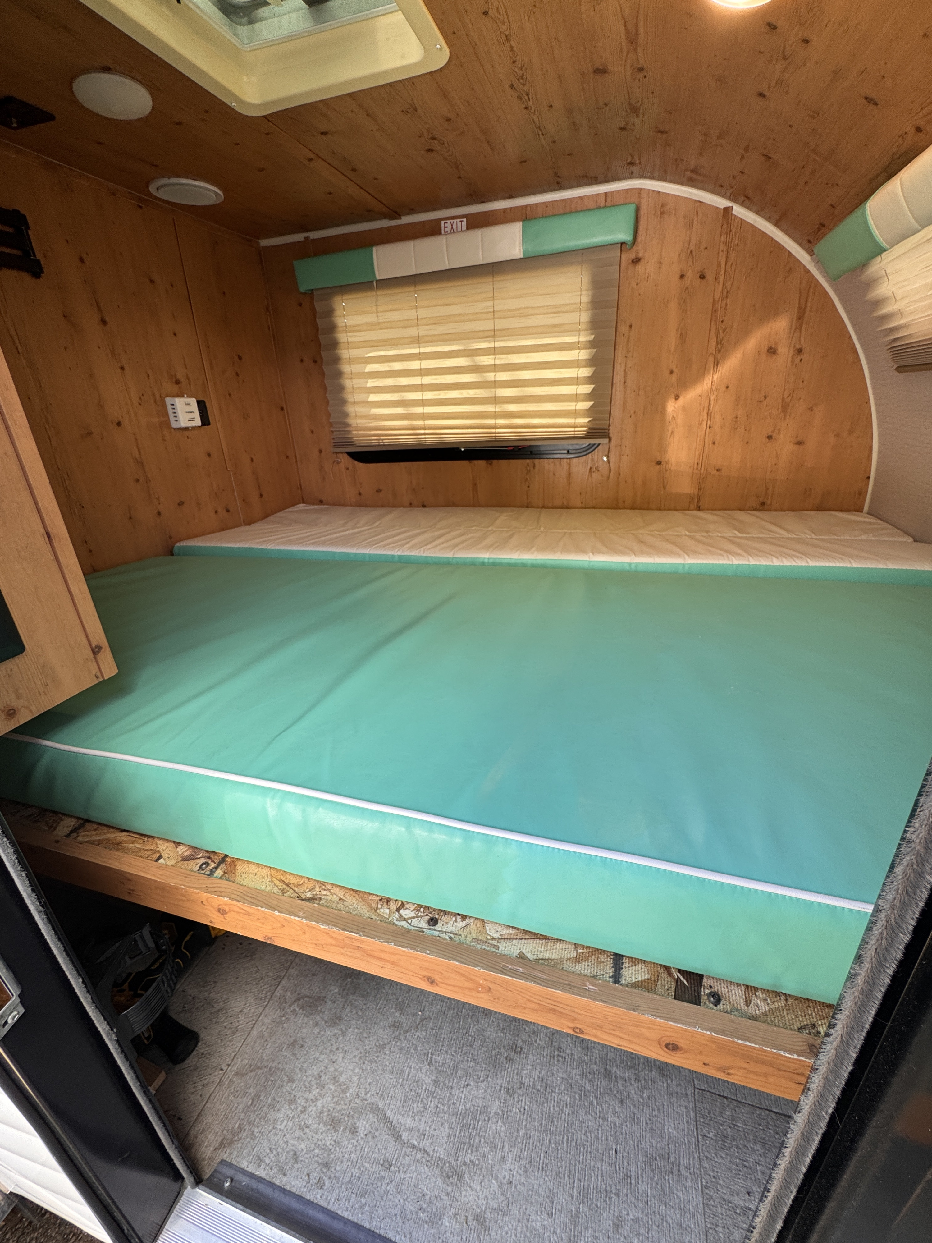 Compact rv rental sleeping area featuring a bright teal mattress on wood paneling, seen from the doorway.. Sunset Park RV SunRay 2022