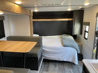 Modern RV rental interior with a cozy bed, dinette, wood-look floor, and sleek dark accents.. Keystone RV Springdale 2022