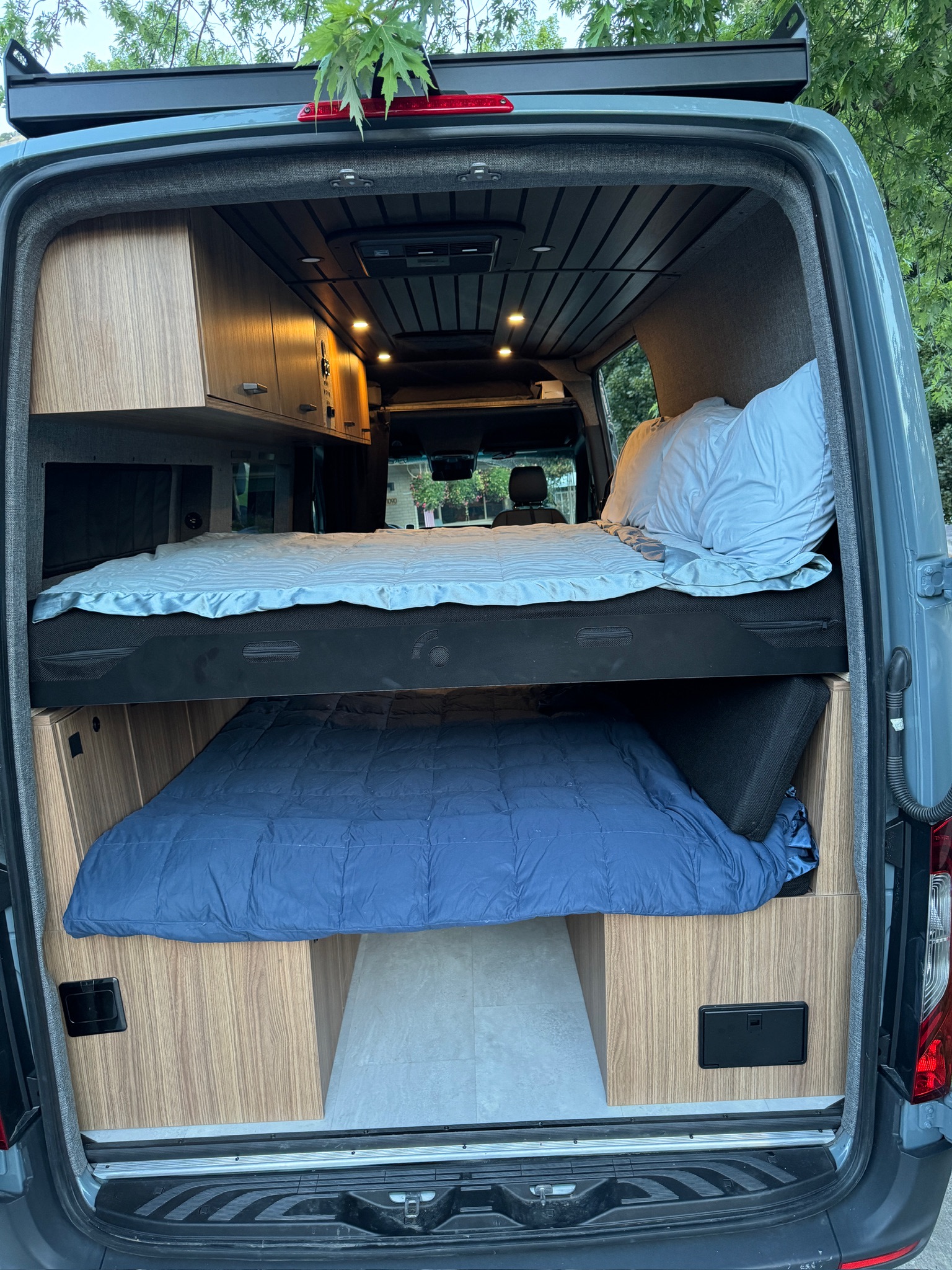RV rental camper van interior shows stacked beds, wood cabinetry, and recessed lighting, ideal for adventurous travel.. Mercedes-Benz Sprinter 2023