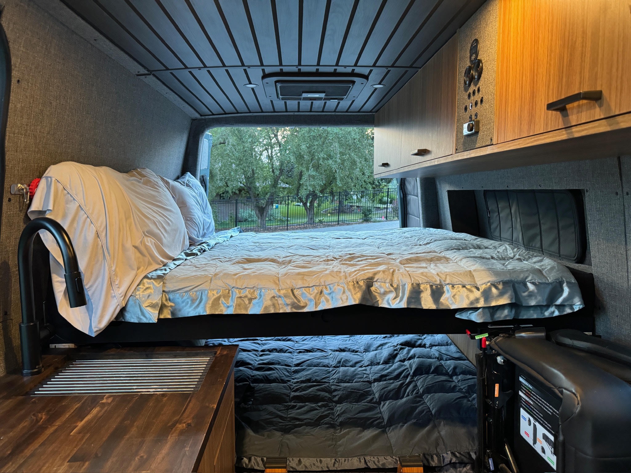 Cozy RV rental interior: elevated bed, lower sleeping area, kitchenette, overhead storage. Ready for your adventure.. Mercedes-Benz Sprinter 2023