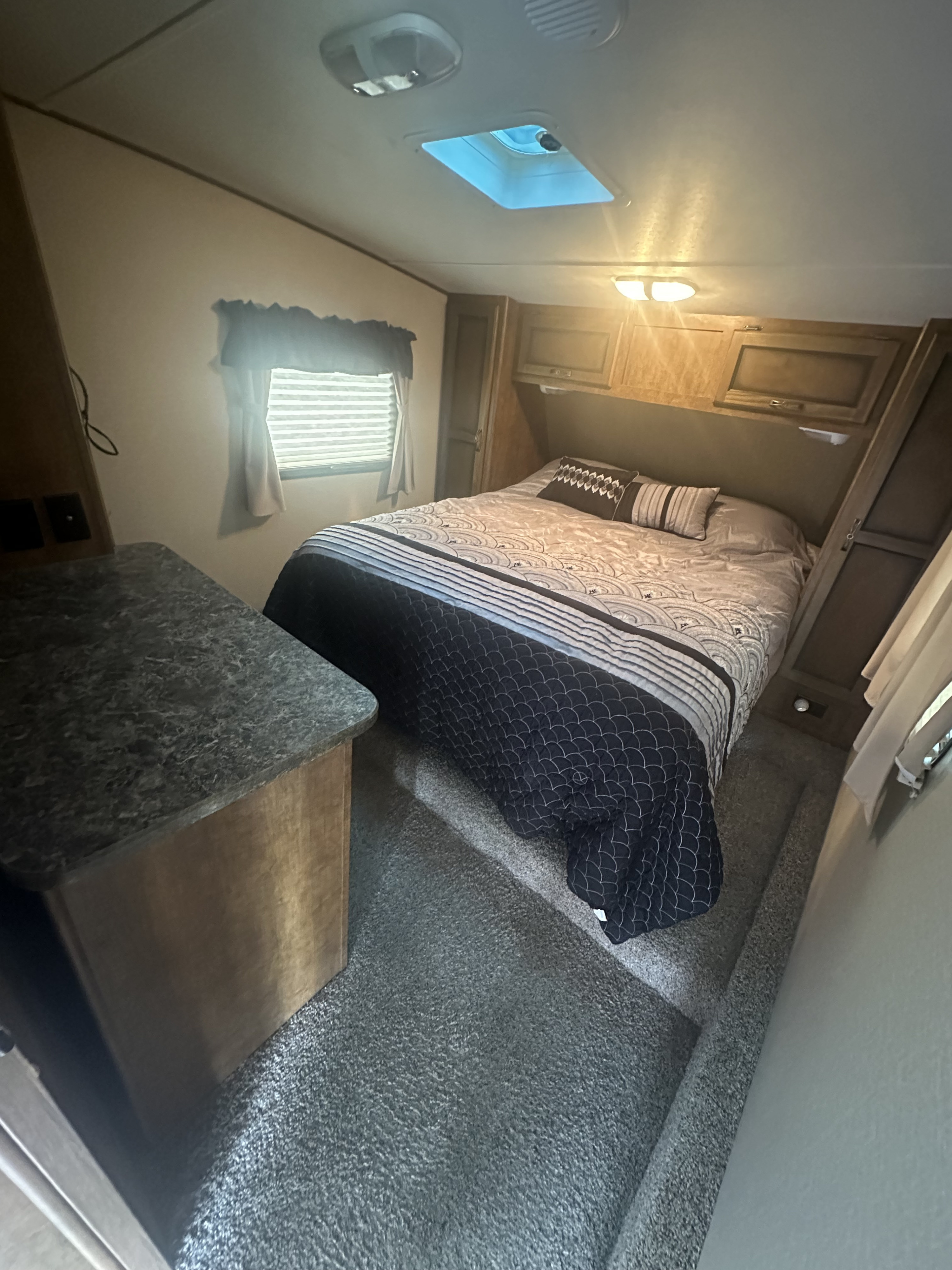 Cozy RV rental bedroom with a comfy bed, patterned bedding, overhead storage, and a window. Perfect for your next adventure.. Crossroads RV Rezerve 2016