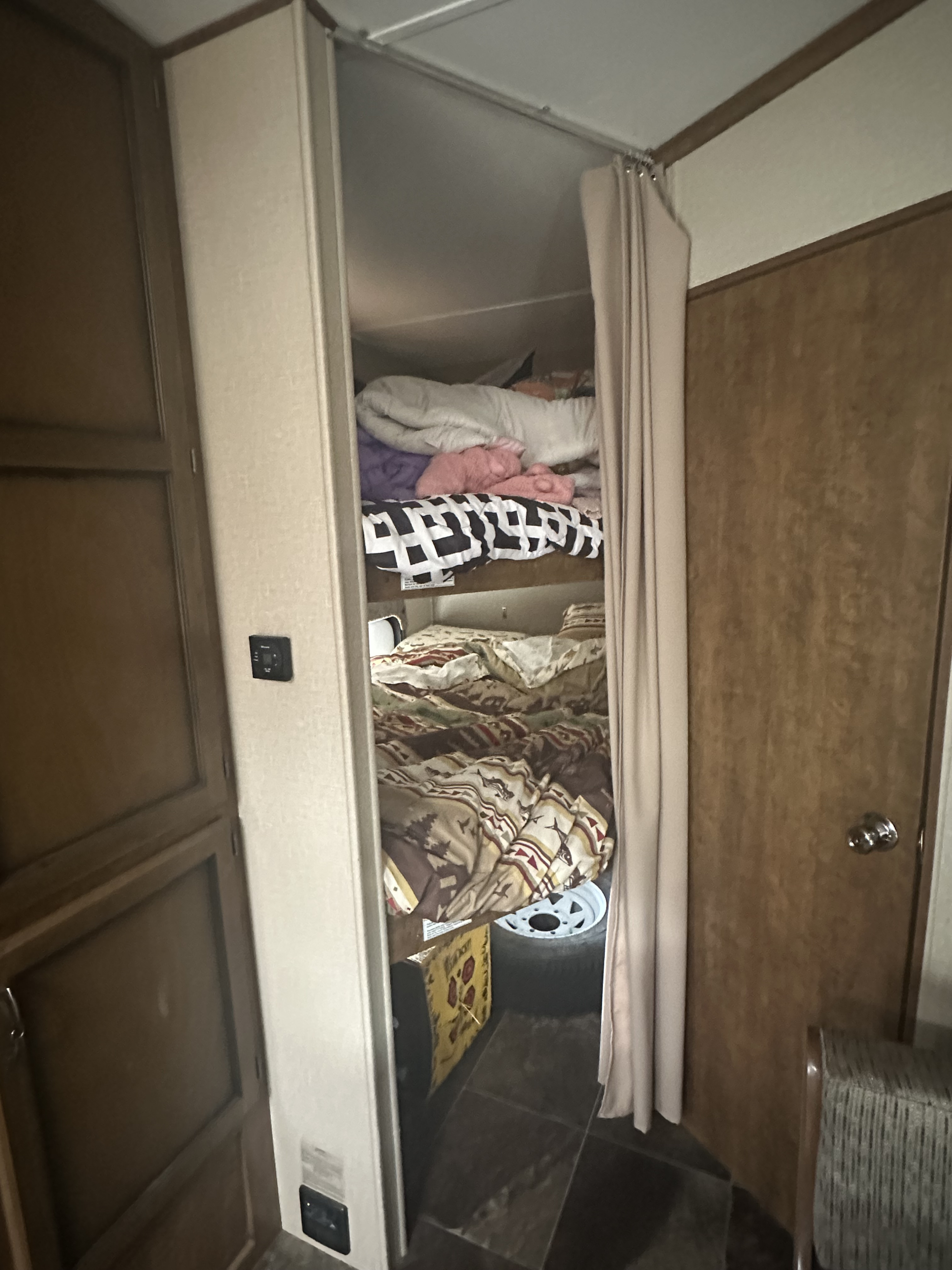 Cozy RV rental interior with two bunk beds, made up with bedding, and a privacy curtain. Includes a wall thermostat and storage space.. Crossroads RV Rezerve 2016