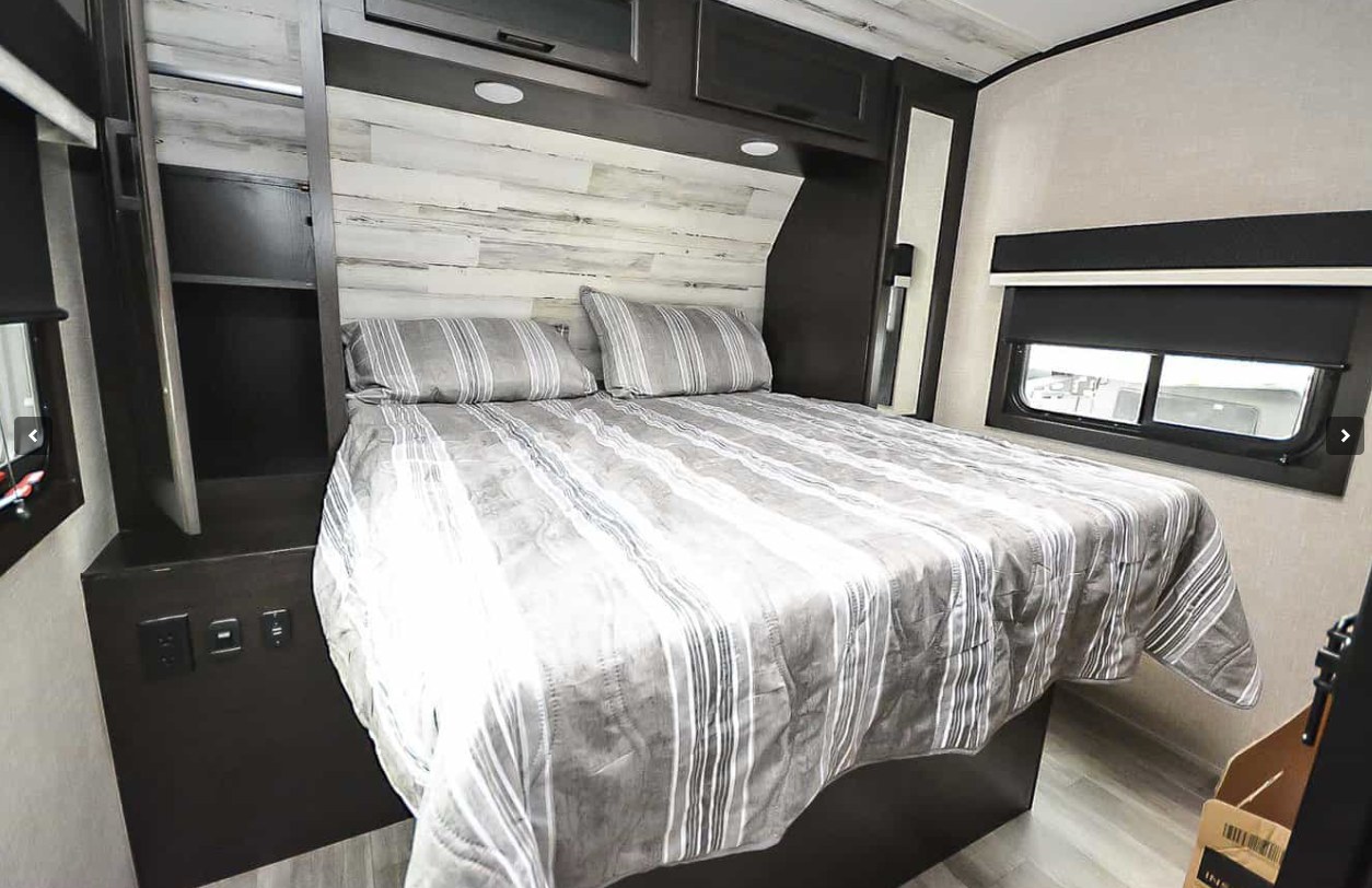 Relax in this modern RV rental bedroom featuring a striped bed, wood paneling, and practical storage for your next adventure.. Jayco Jay Feather 2023