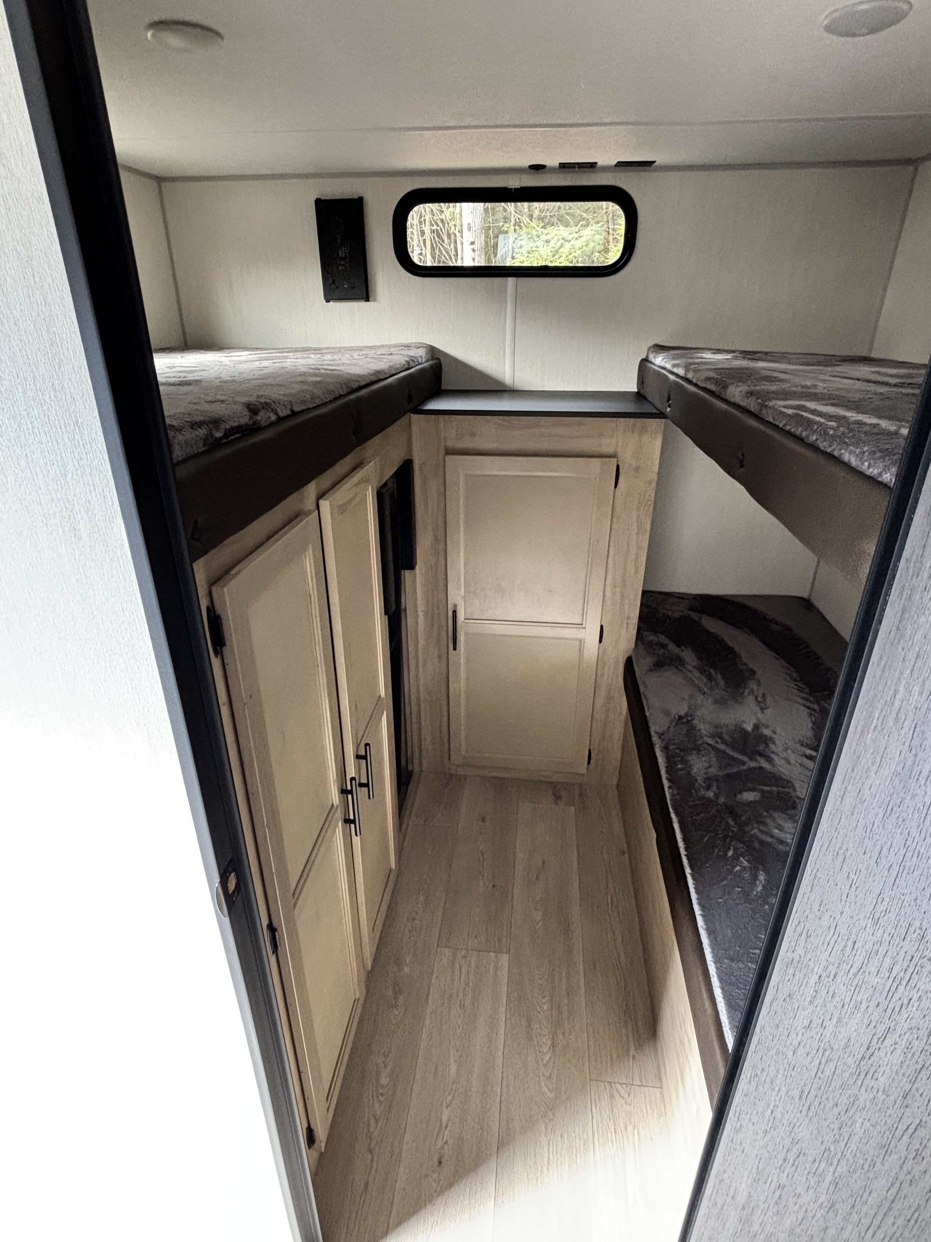 This RV rental bunkhouse interior features light wood-look flooring and cabinets, with comfy twin bunks on both sides, ideal for travel and camping.. Forest River Cherokee Grey Wolf 29TE 2026