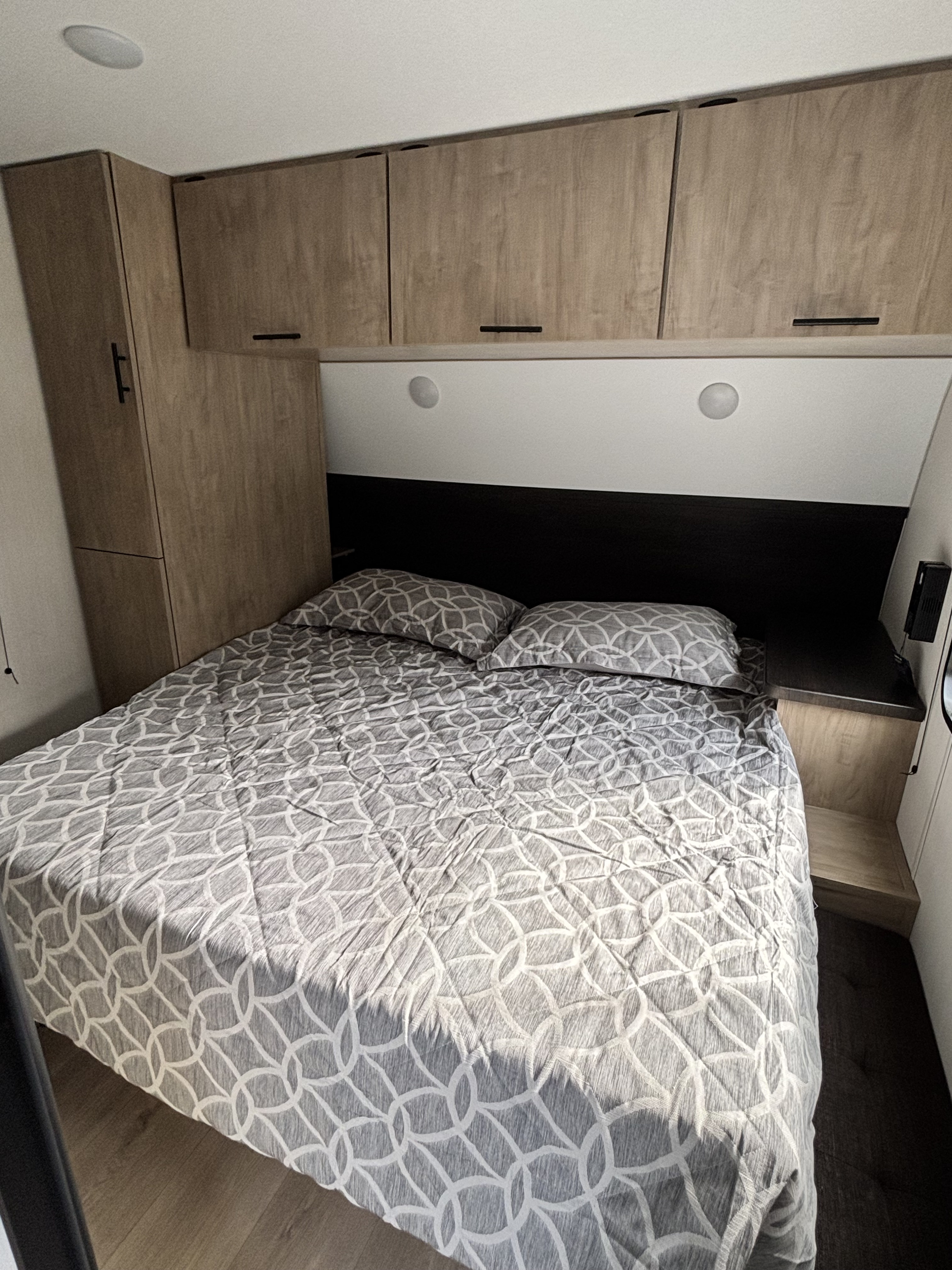 Compact RV rental bedroom featuring a comfy bed with patterned bedding, overhead cabinets, and built-in lighting.. Forest River Cherokee Grey Wolf 29TE 2026