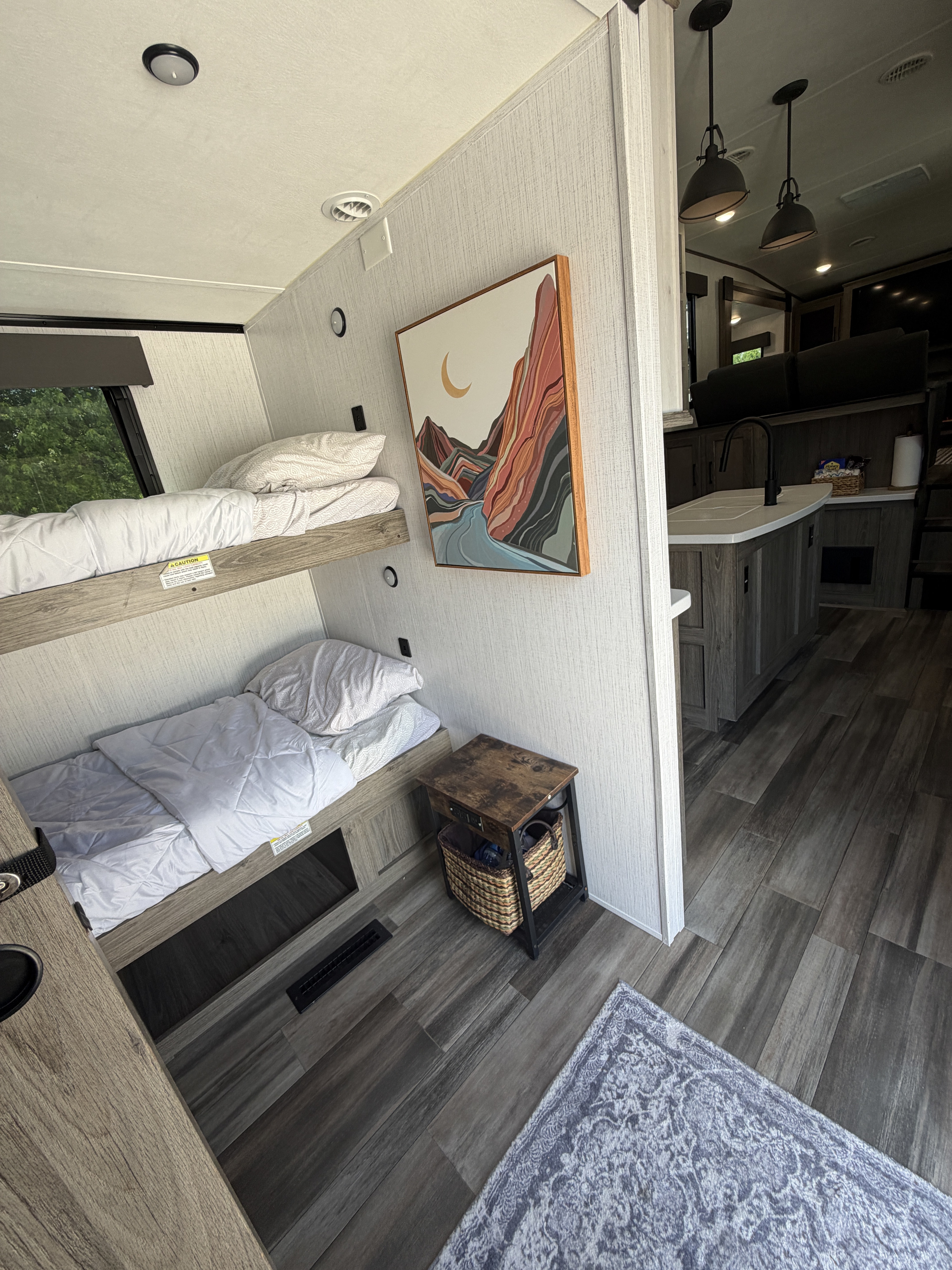 This rv rental features comfy bunk beds with white linens, a scenic art piece, a partial view of the kitchen island, and wood flooring.. Heartland RVs Milestone 2022