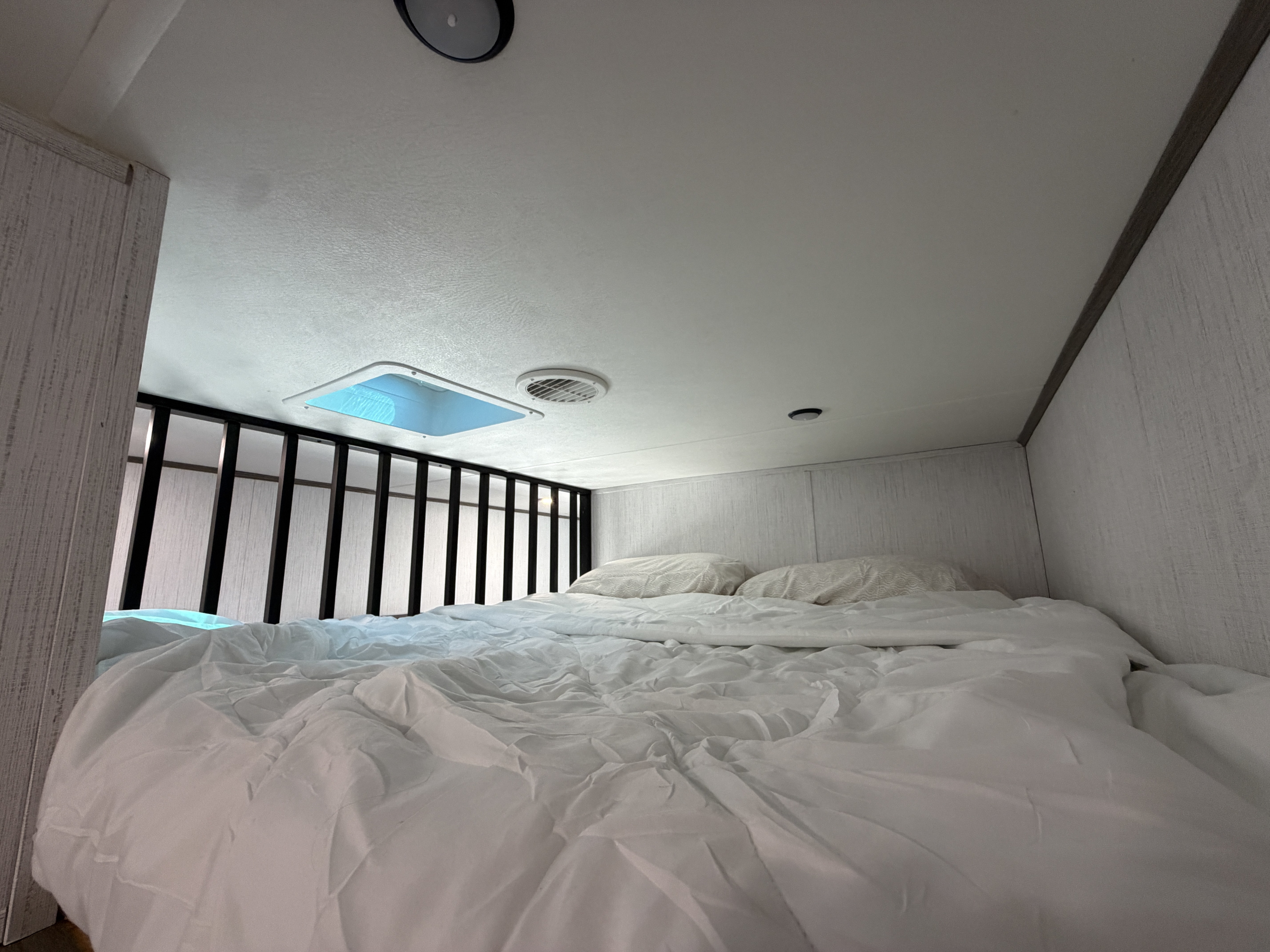 RV rental's cozy sleeping area: bed with white bedding, pillows, ceiling vent, and bright skylight.. Heartland RVs Milestone 2022