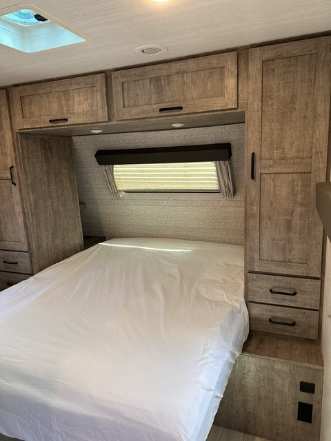 Comfortable RV rental bedroom featuring a large bed, overhead cabinets, and side storage, perfect for your next adventure.. Forest River Surveyor Legend 276BHLE 2024