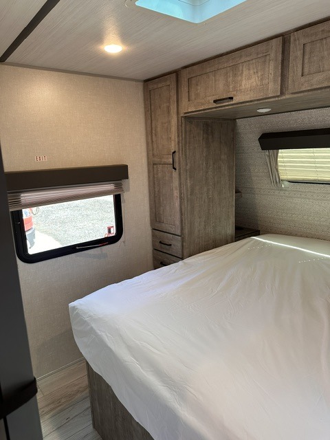 Clean, modern RV rental bedroom with a comfortable bed, overhead wood cabinets, and an emergency exit window.. Forest River Surveyor Legend 276BHLE 2024